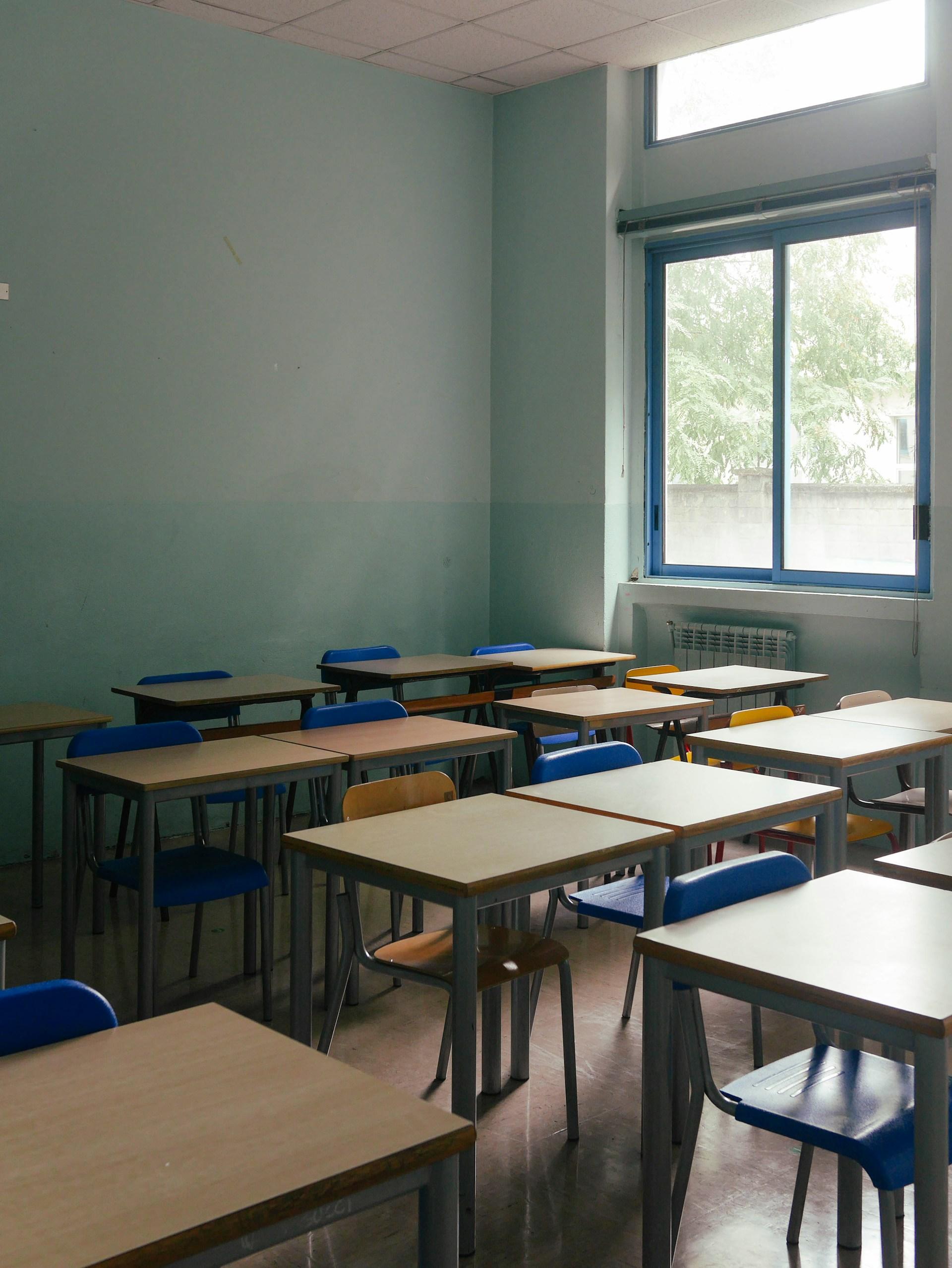 A classroom empty of students, with desks arranged in rows with blue chairs tucked into them. 