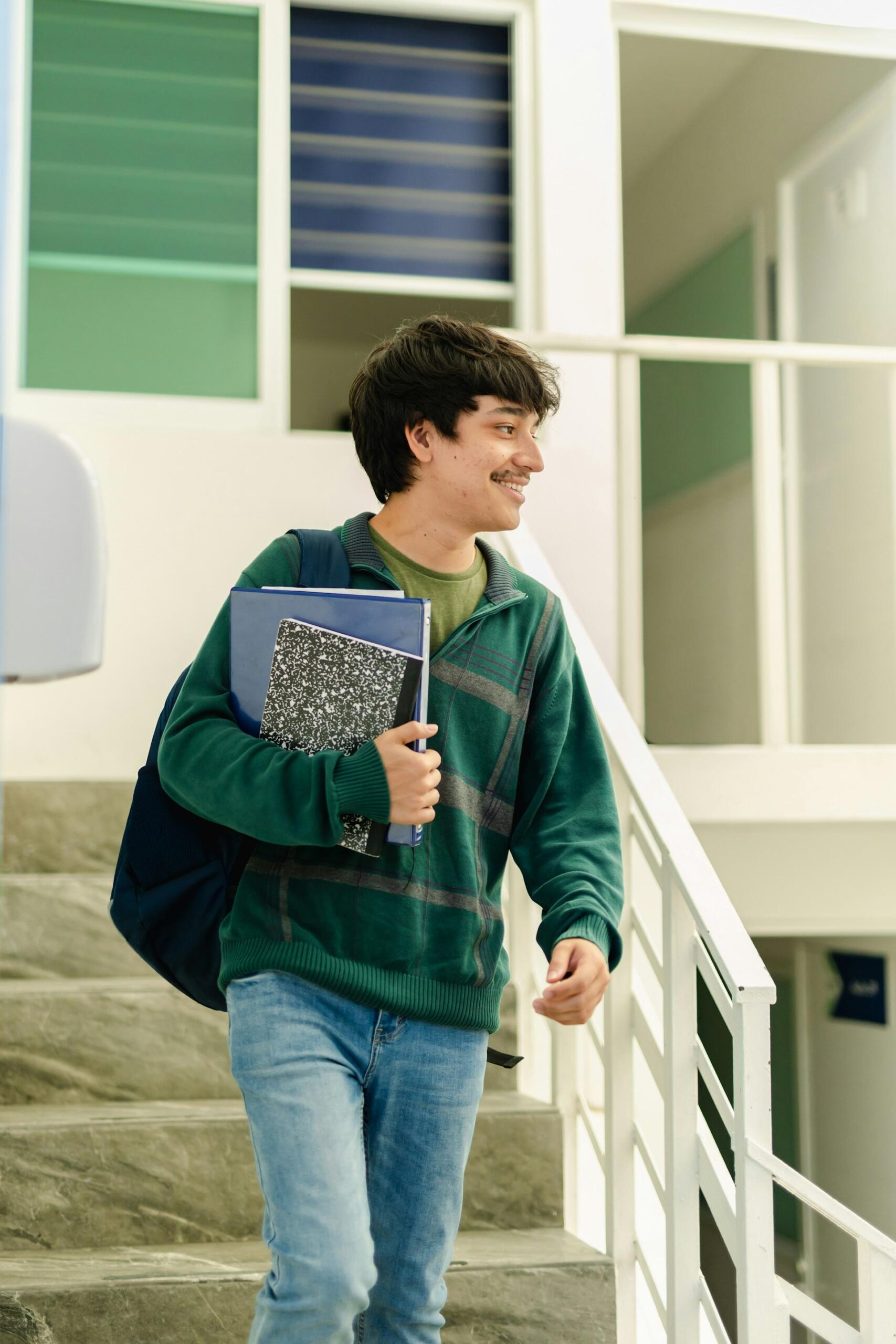 A person wearing a green jumper and holding school books on a sunny day. 