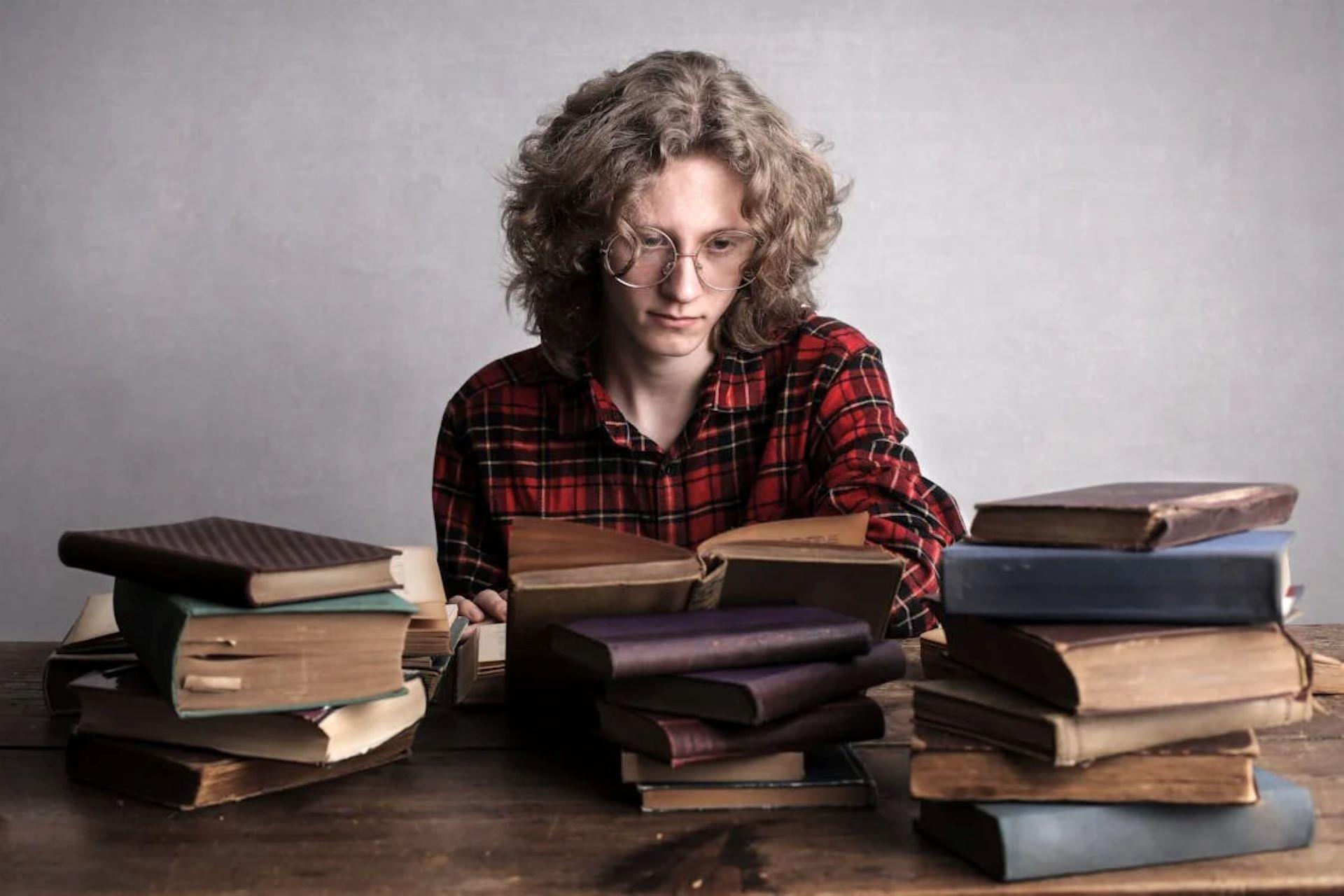 Male student at a table with a pile of books.