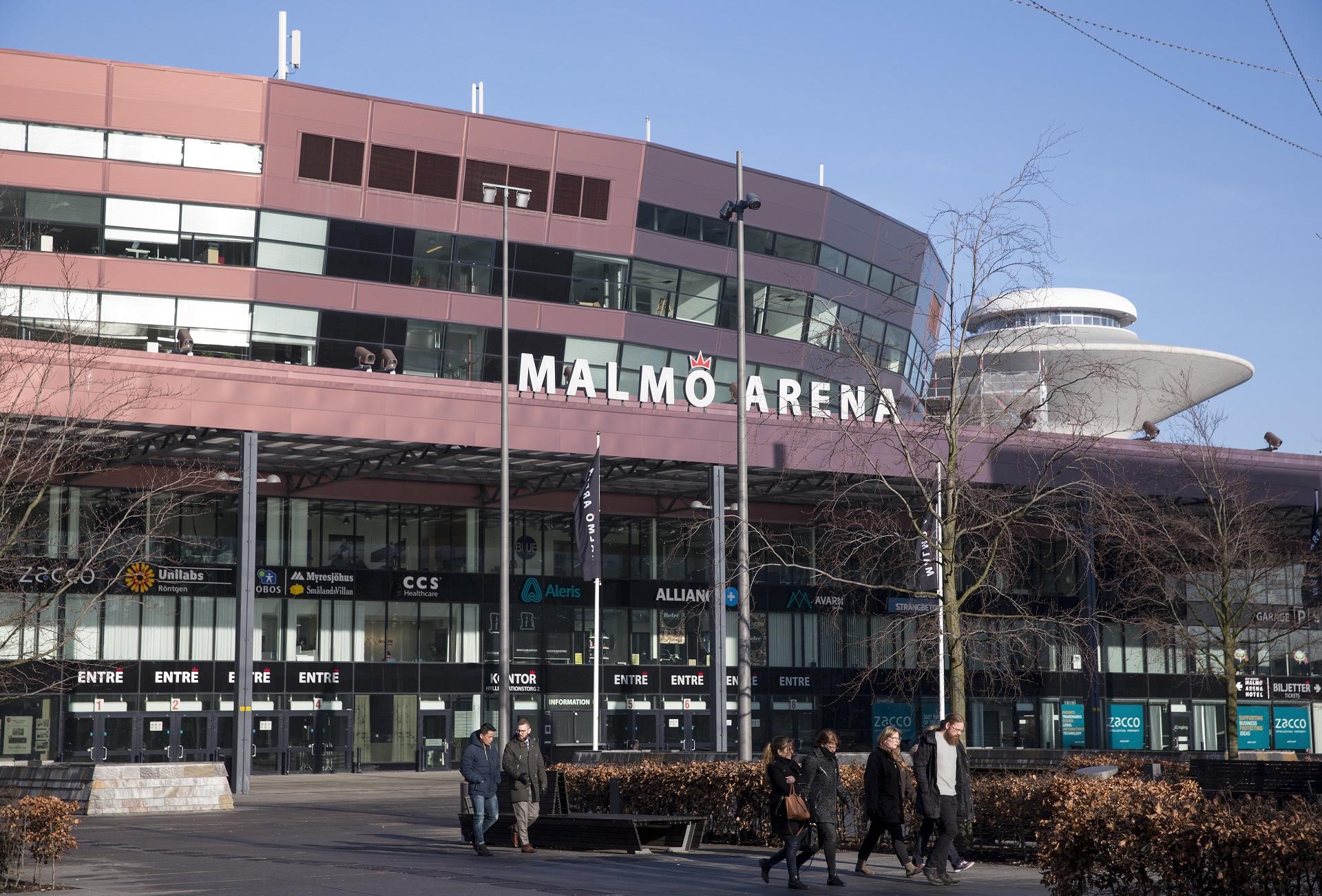 The front entrance of the Malmo Arena in daylight, under a clear blue sky. 