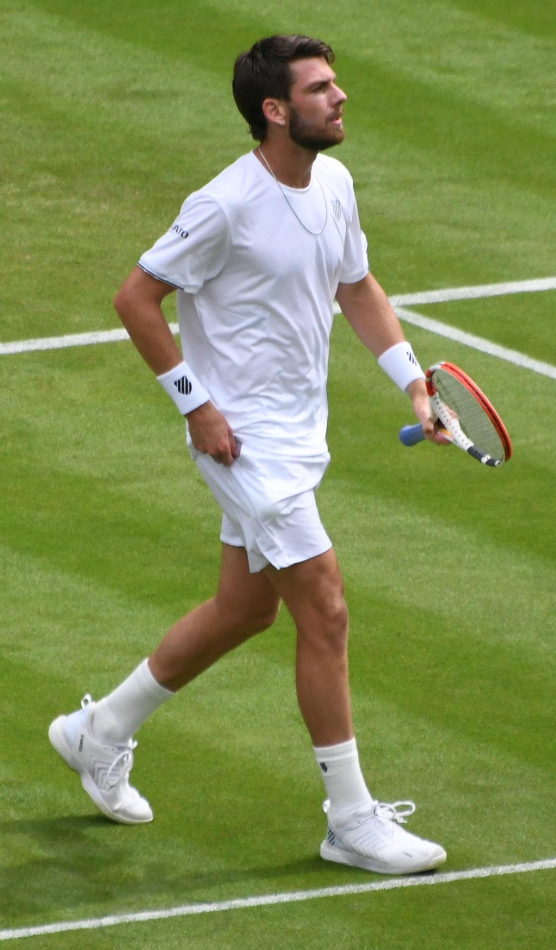 A person in tennis whites strides across a lawn court with racket in hand