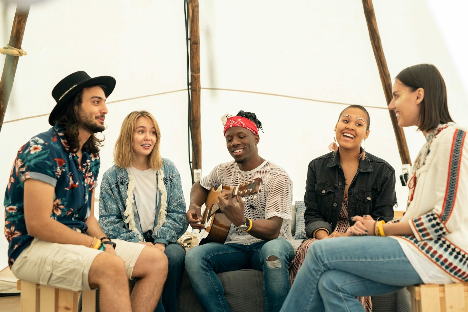 A group of casually-dressed young people sit under a white awning in a semi-circle.