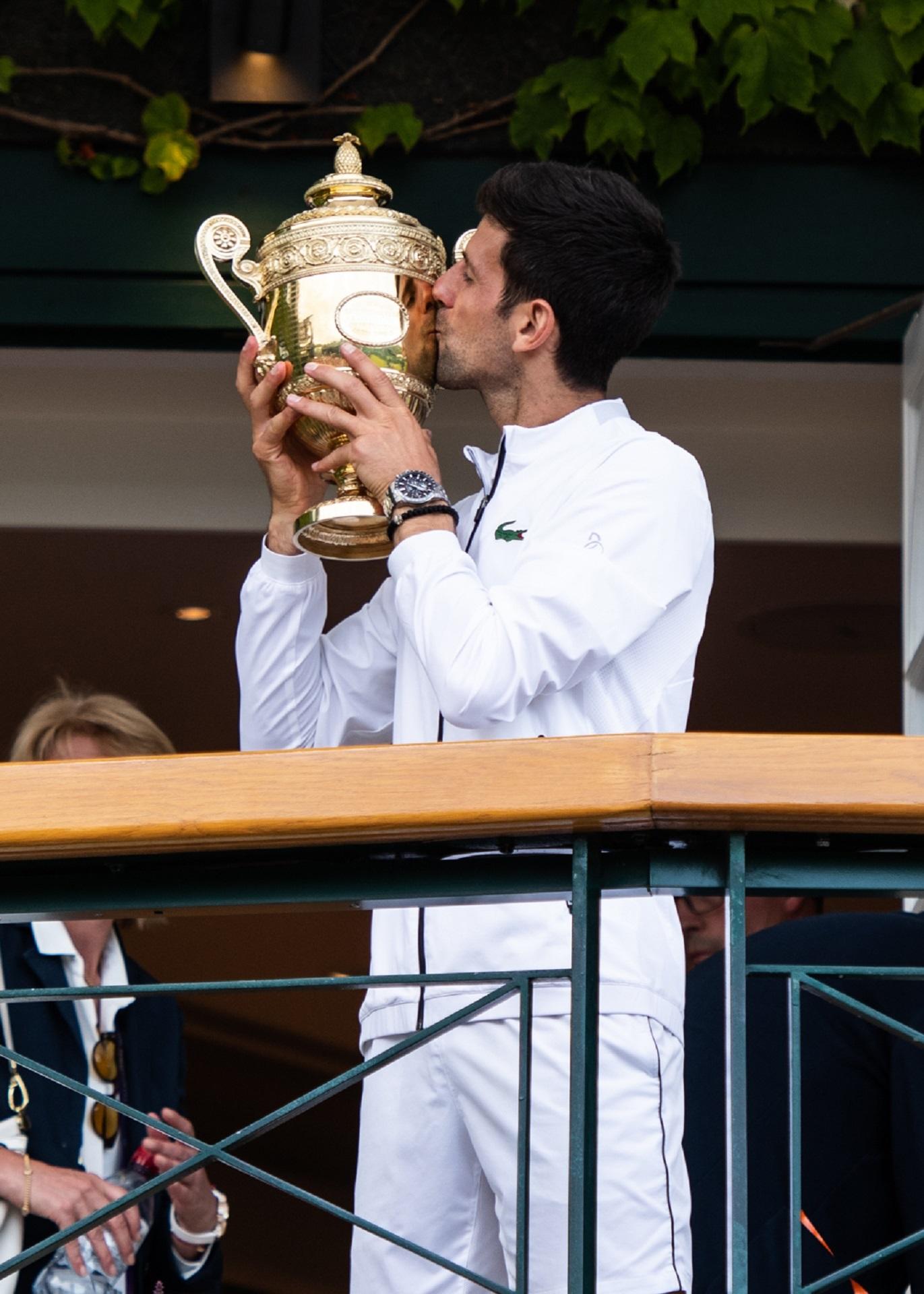A person wearing white holds a gold trophy up and kisses it. 