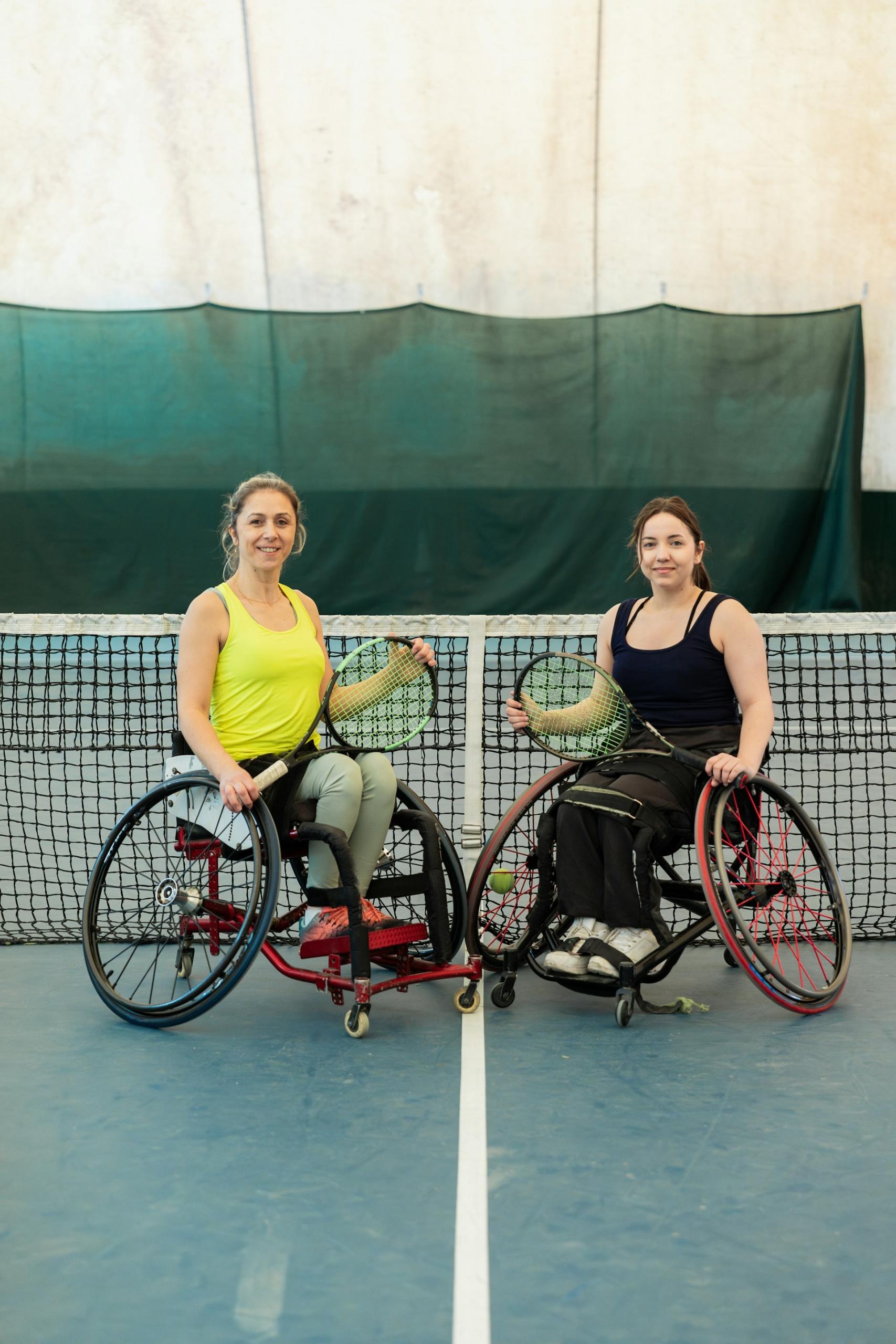 Two women in wheelchairs on a tennis court in front of the net.