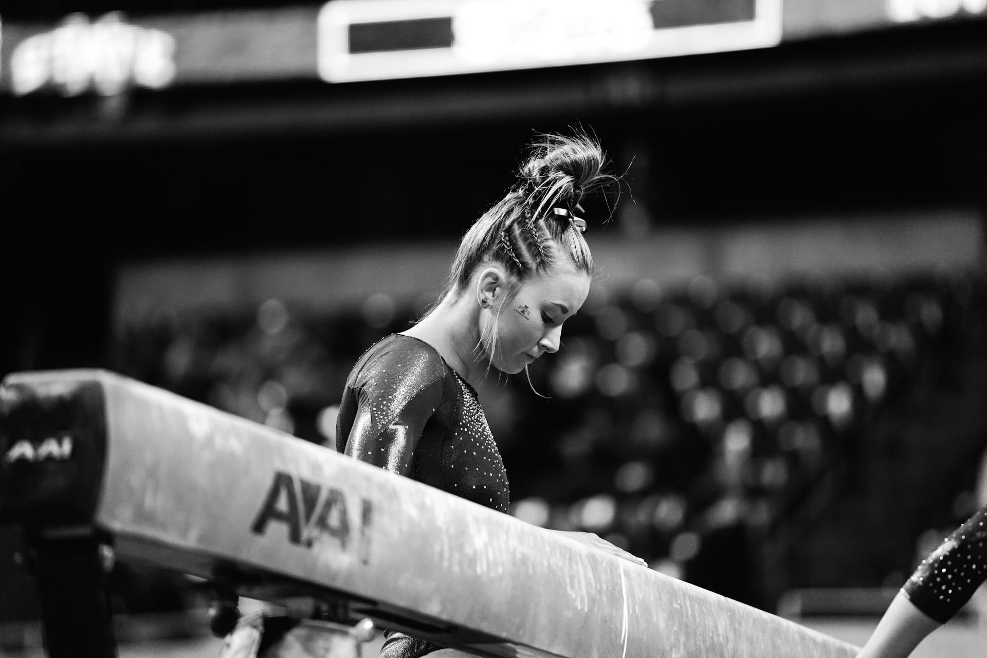A gymnast standing beside a balance beam.