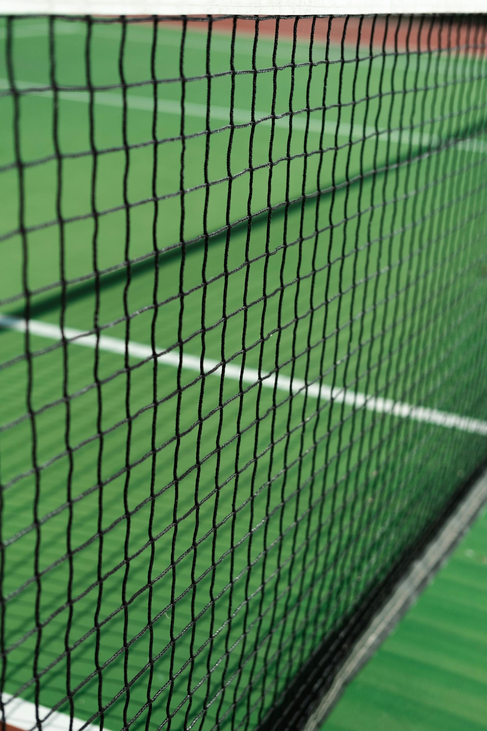 A close-up of a black net strung across a green tennis court.