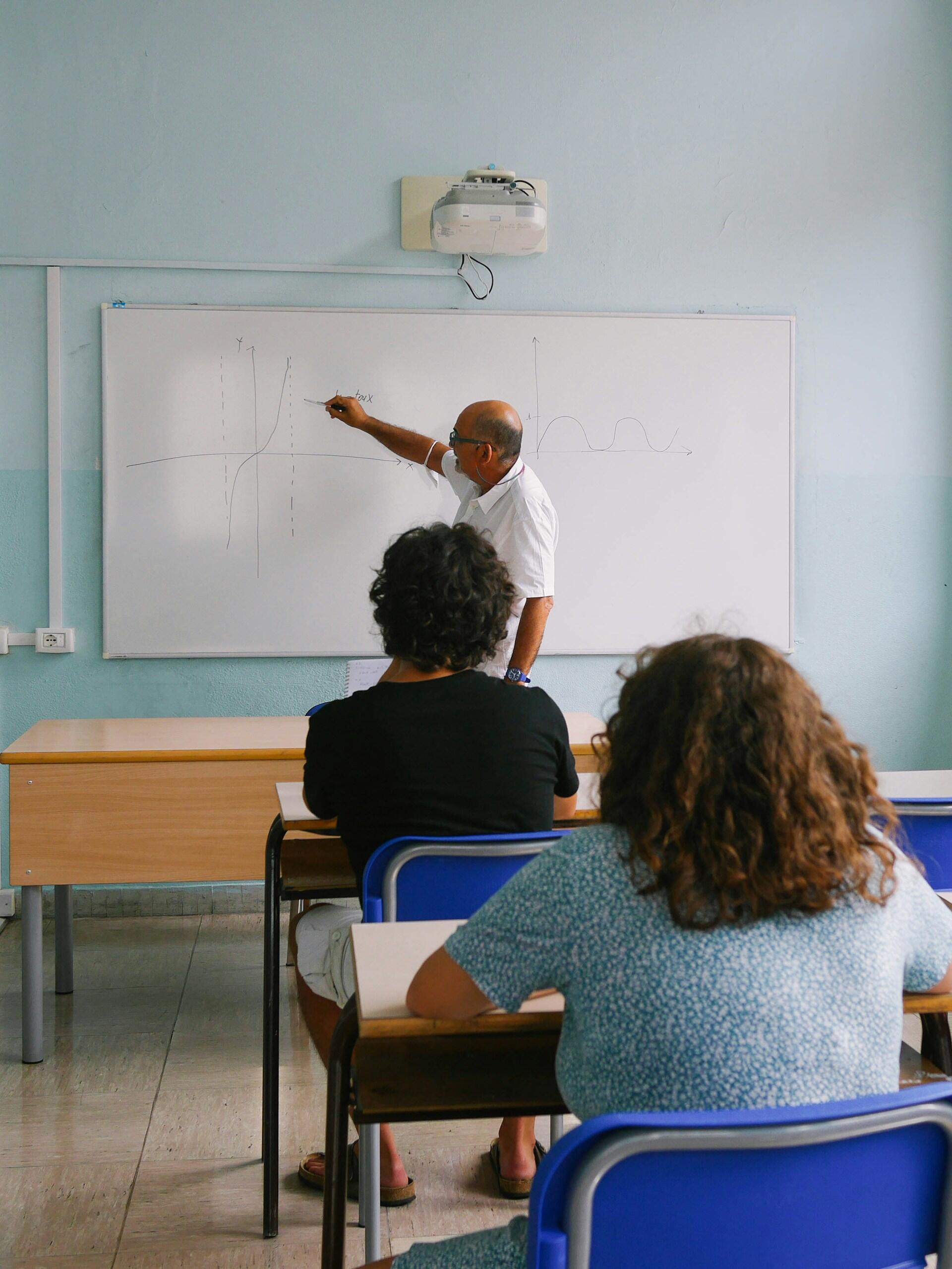 A person in a white shirt stands at a whiteboard while students look on. 