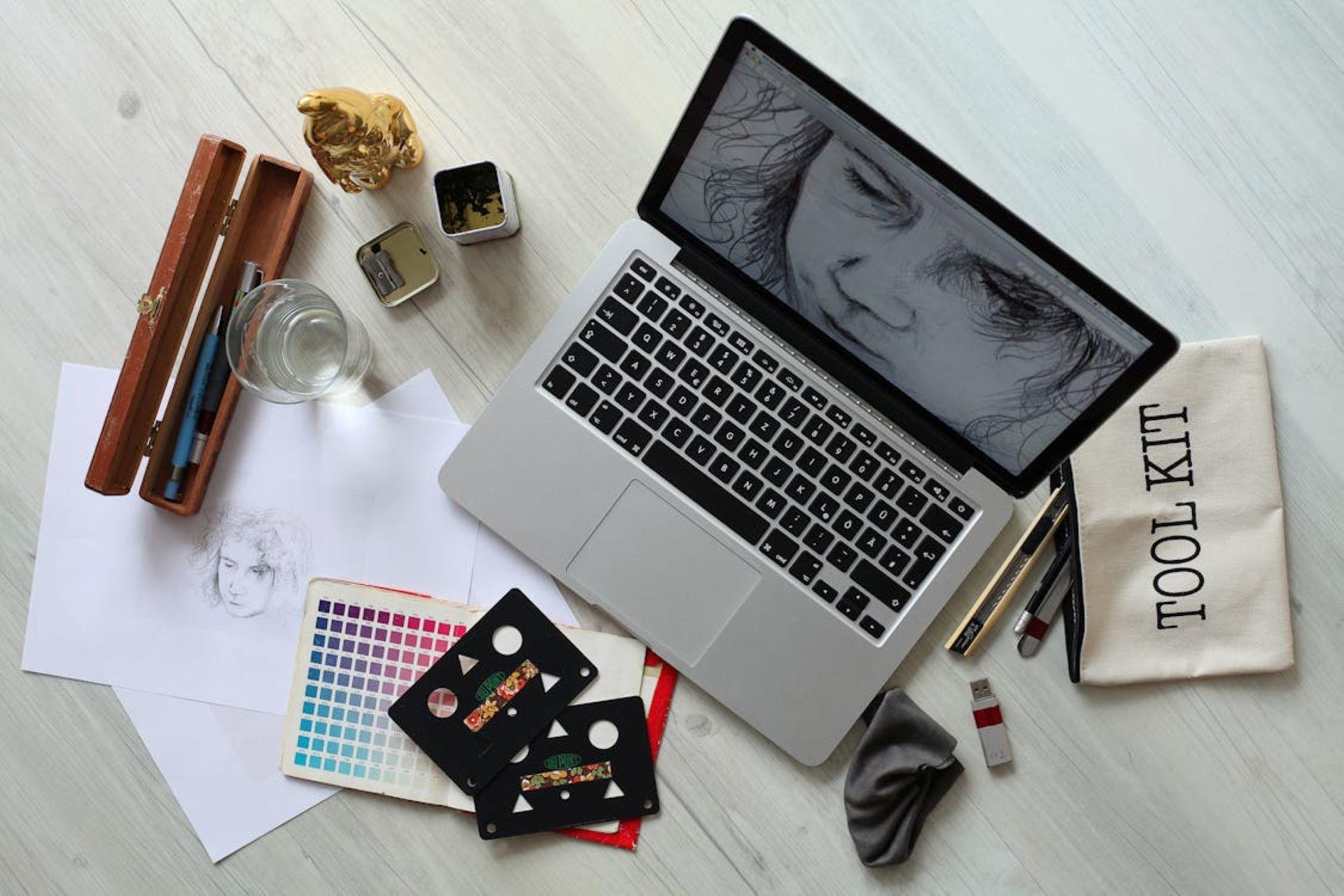 A laptop computer with pencils and a sketchbook on a desk.