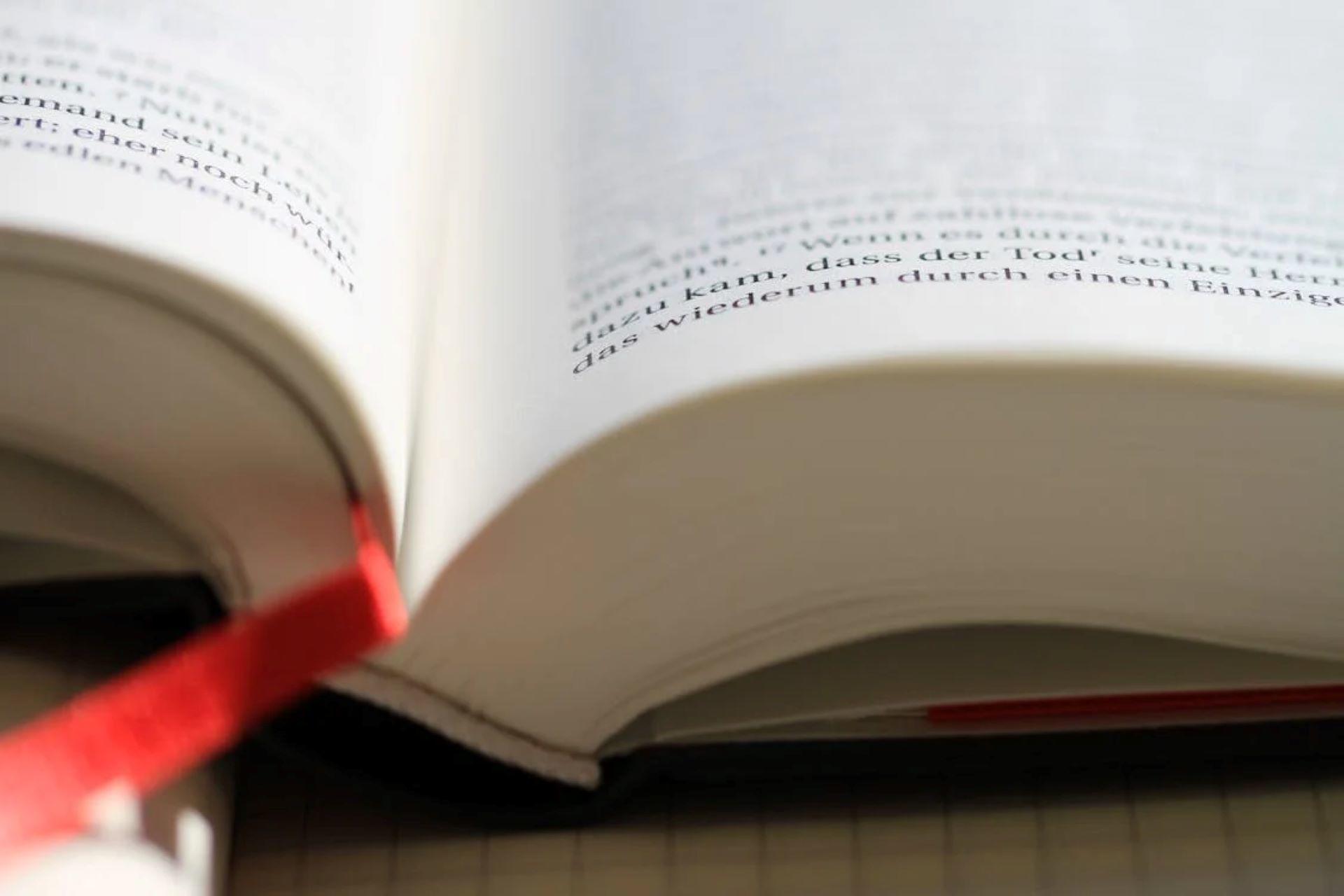 Open book with a red ribbon bookmark on a table.