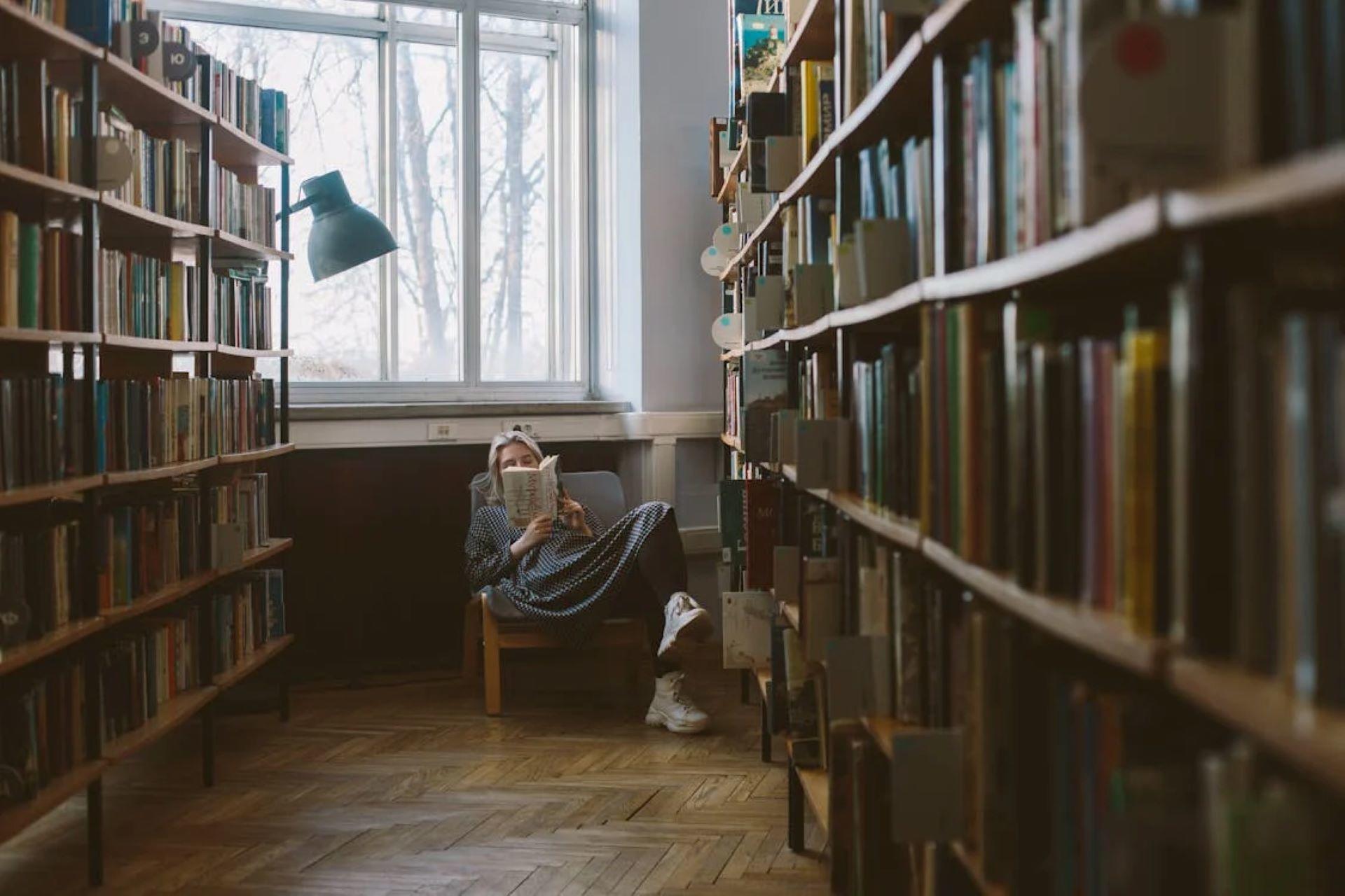 Woman reading a book in a library surrounded by bookshelves.
