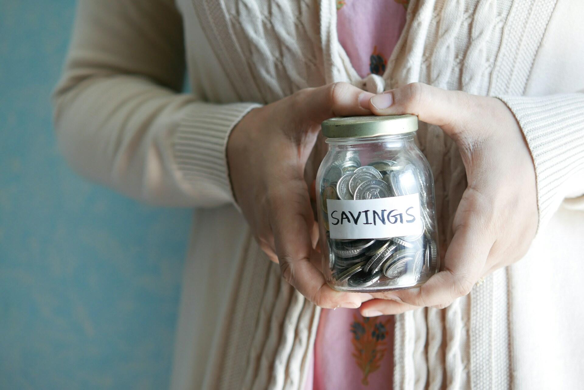 A person holding a glass jar full of silver coins. 