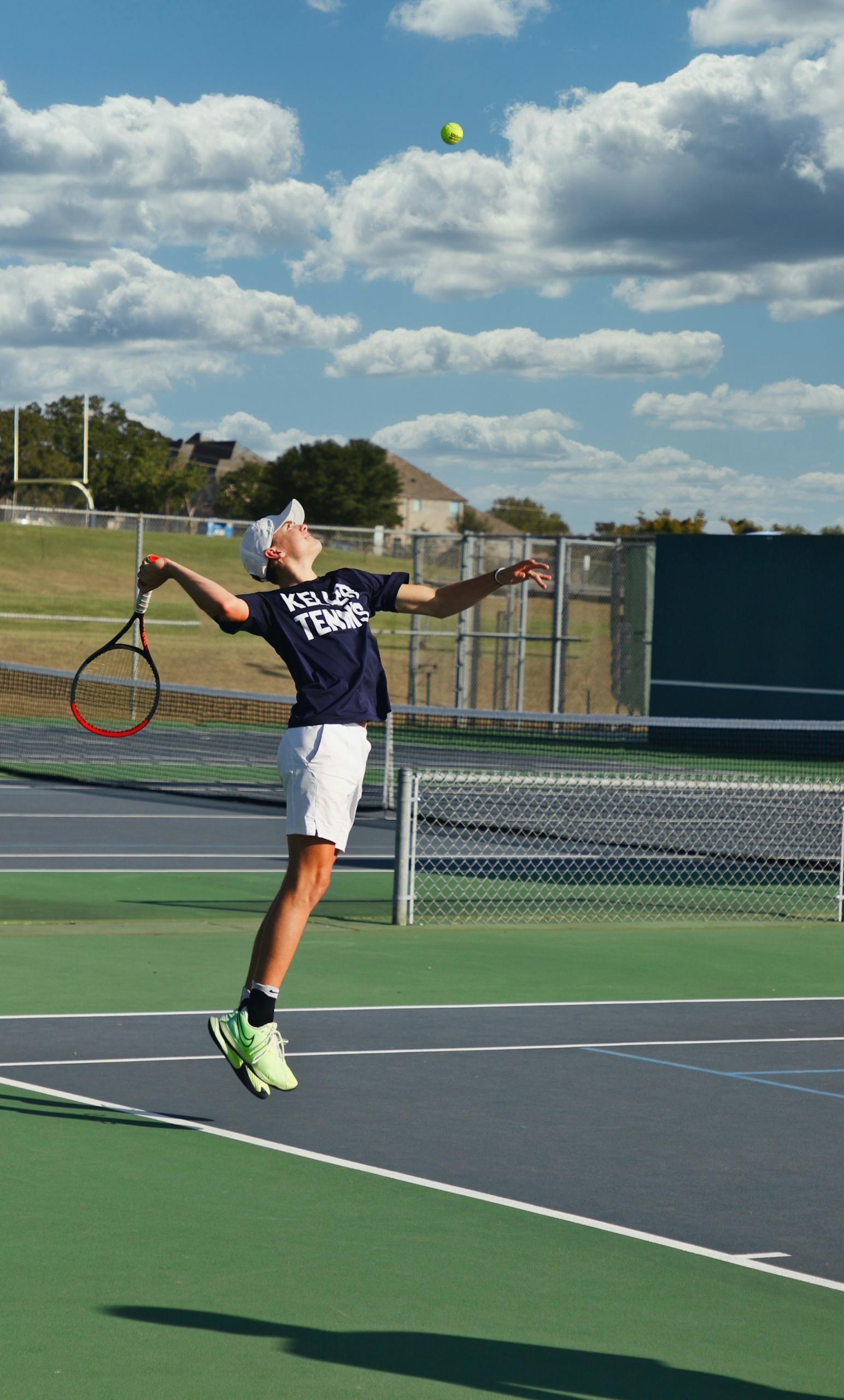 A person wearing a blue shirt and white shorts plays tennis outdoors on a mildly cloudy day.