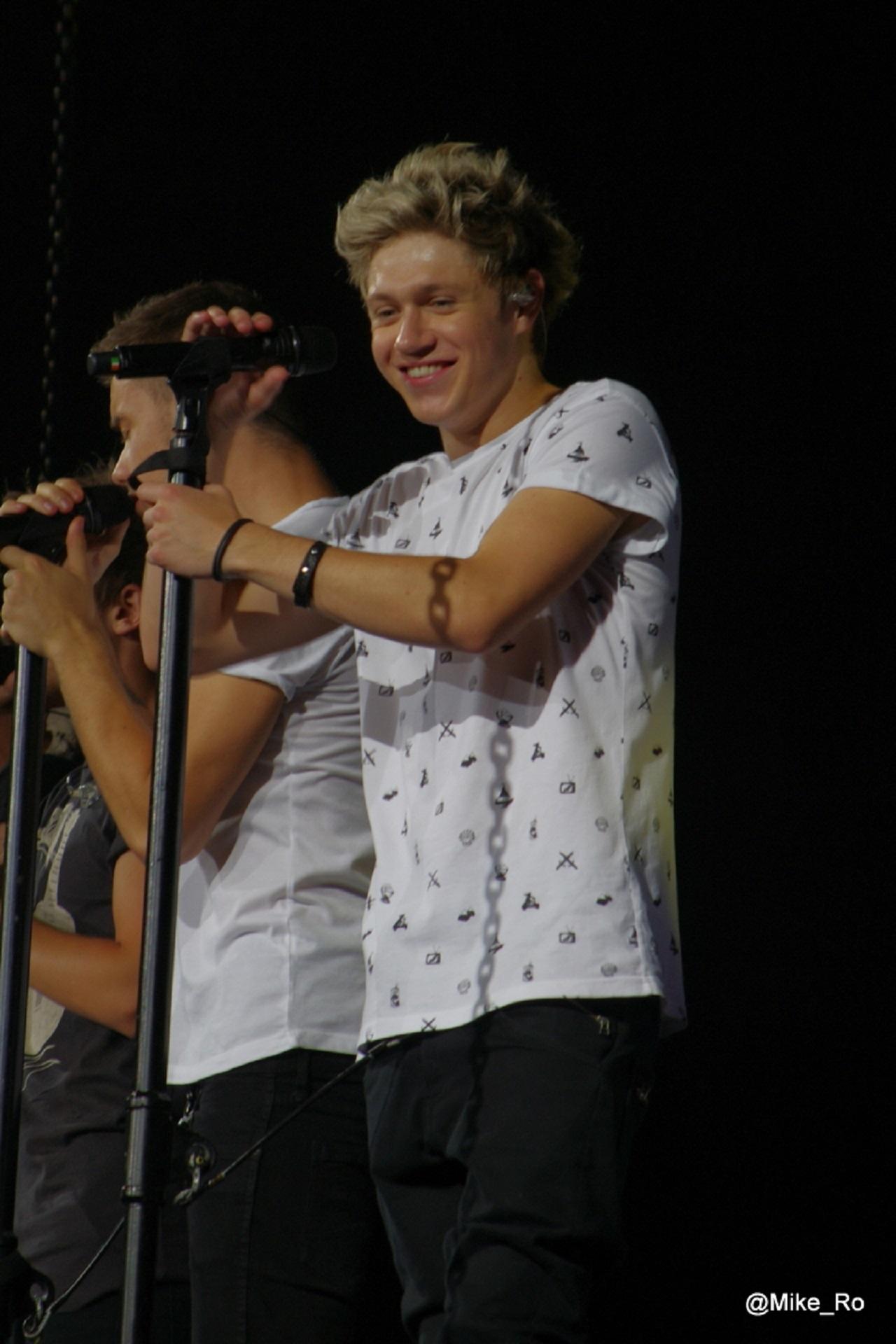 A youth in a white tee shirt smiles as he clings to a microphone stand, while grasping the microphone with the other 
