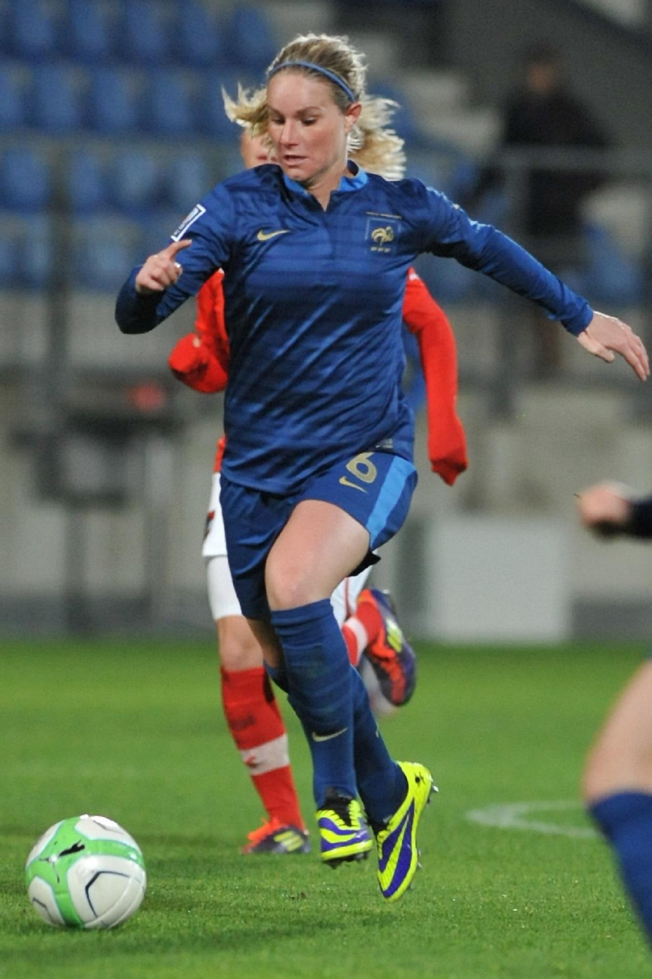 A person wearing a royal blue sports uniform leaps to kick a ball.