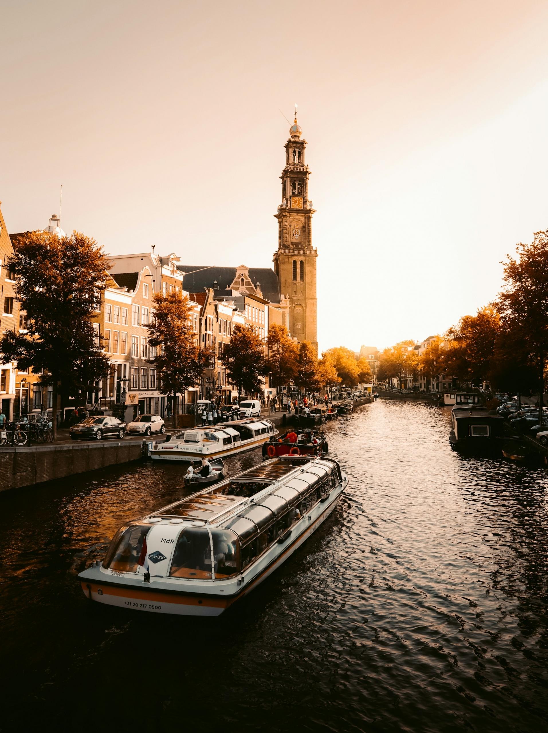 The sun sets on a canal with a boat travelling on it.