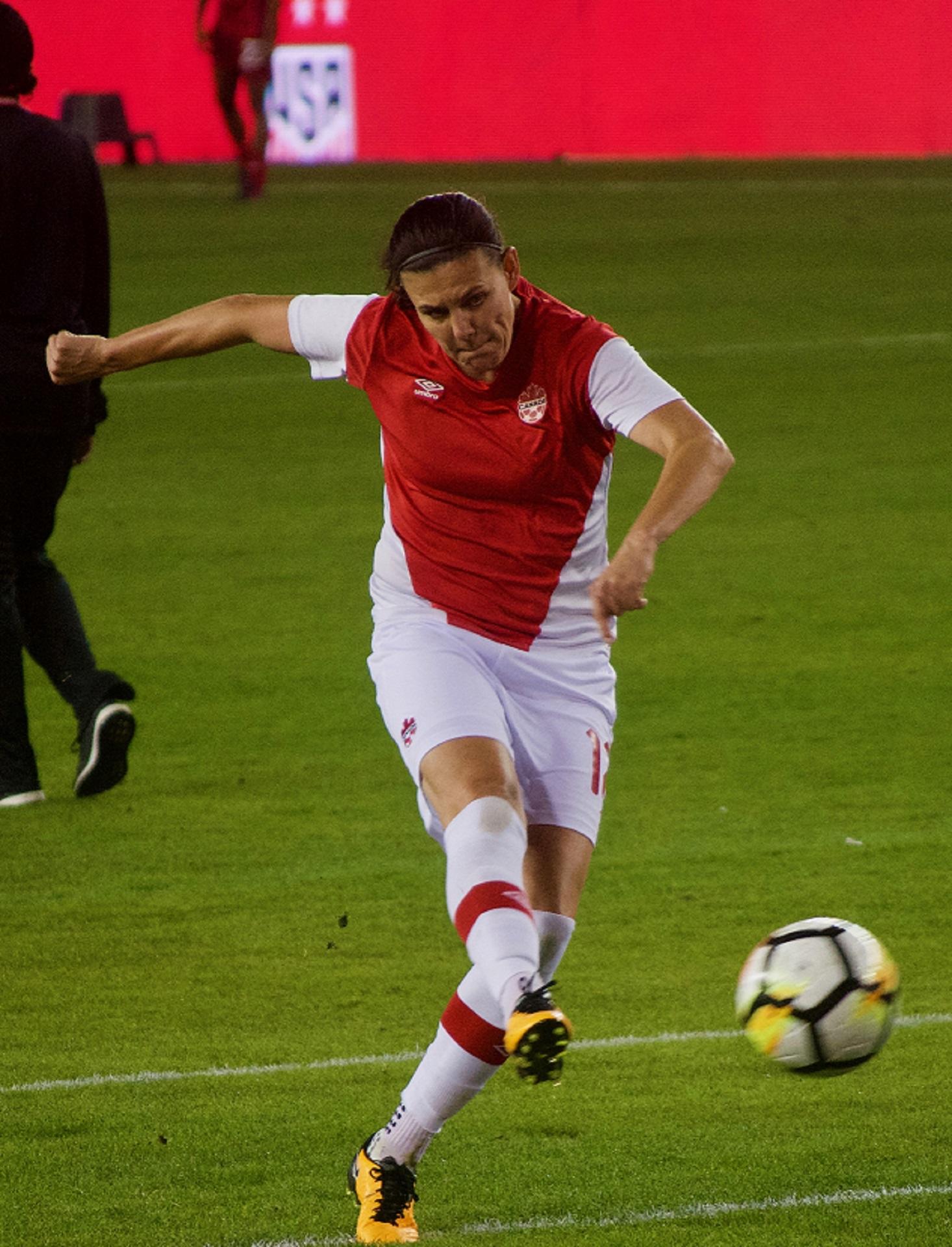 A person in a red and white sports uniform kicks a football on a pitch.