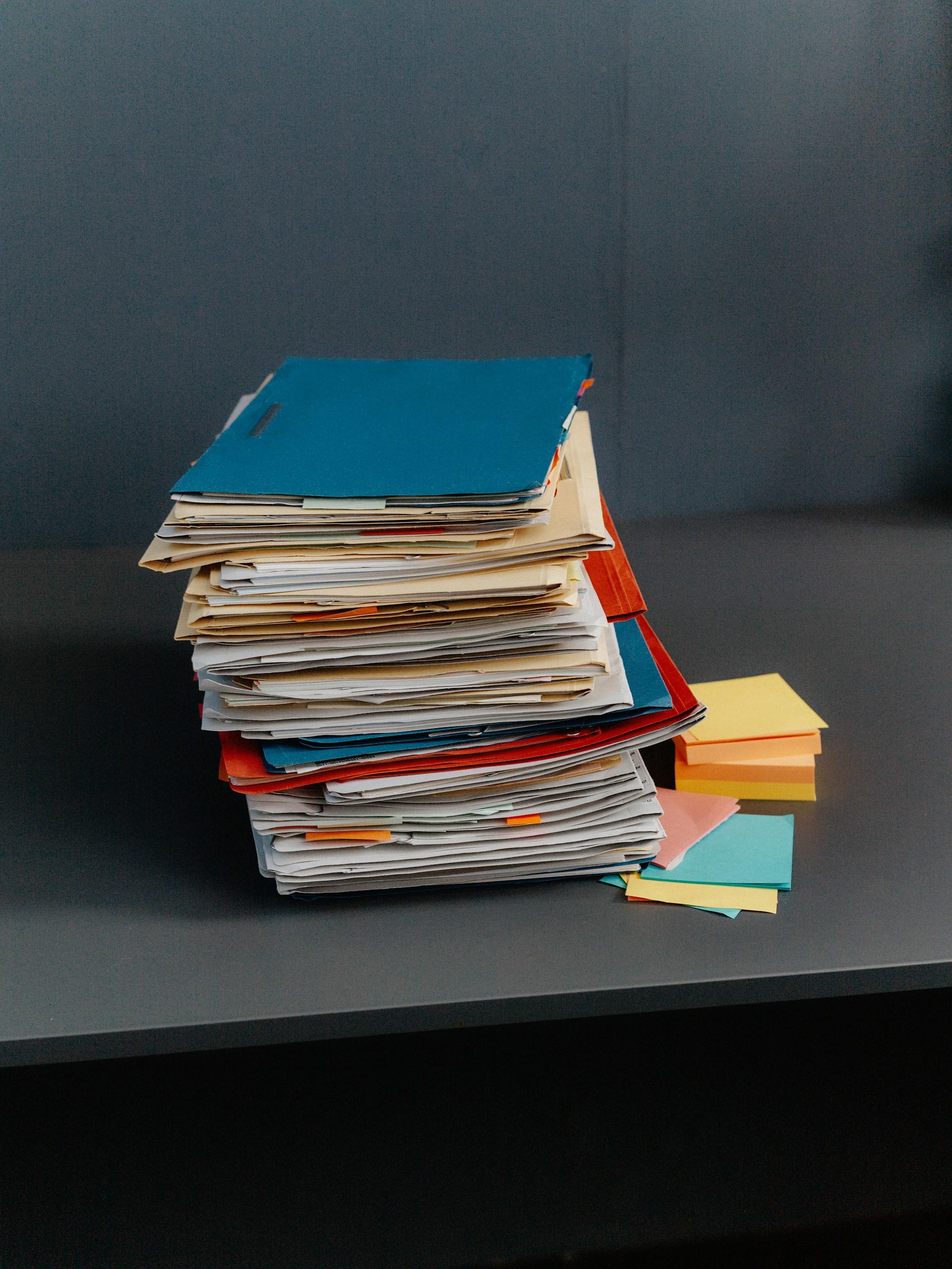 A stack of folders and sticky notes on a grey table. 
