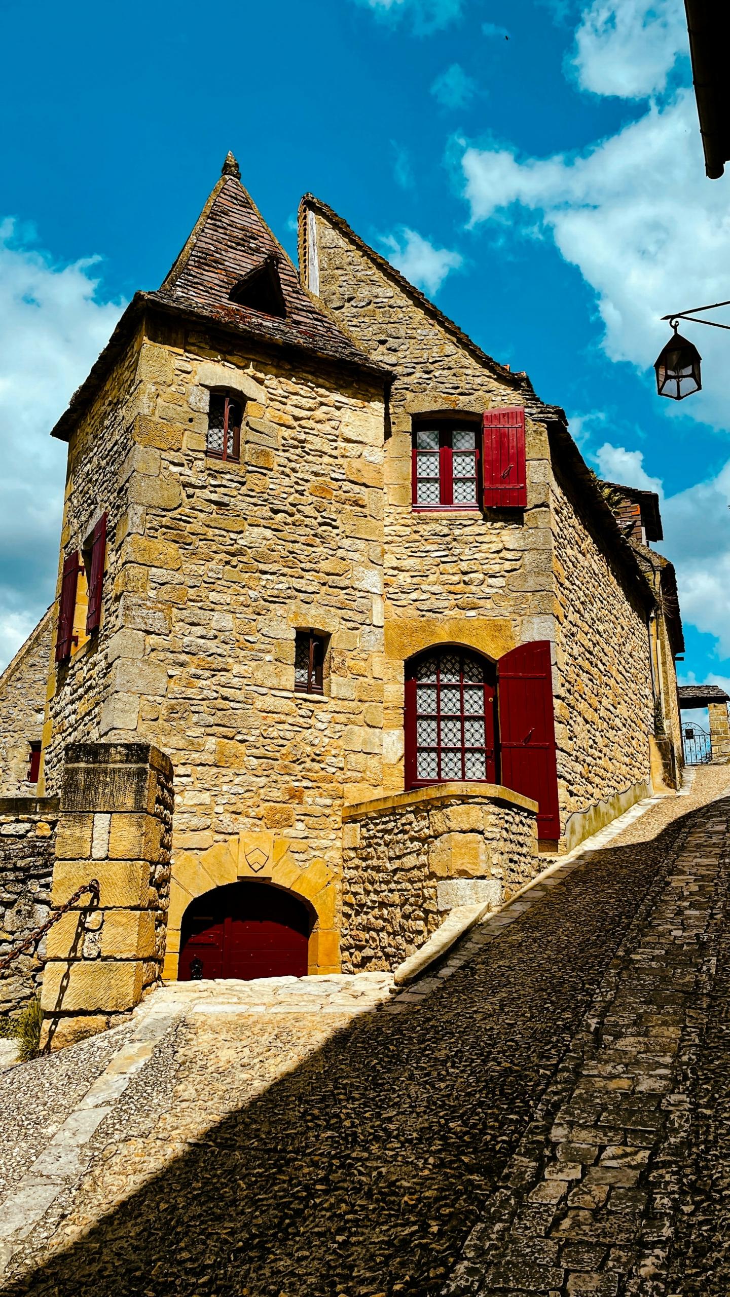 A large stone building with red shutters on a sunny day.