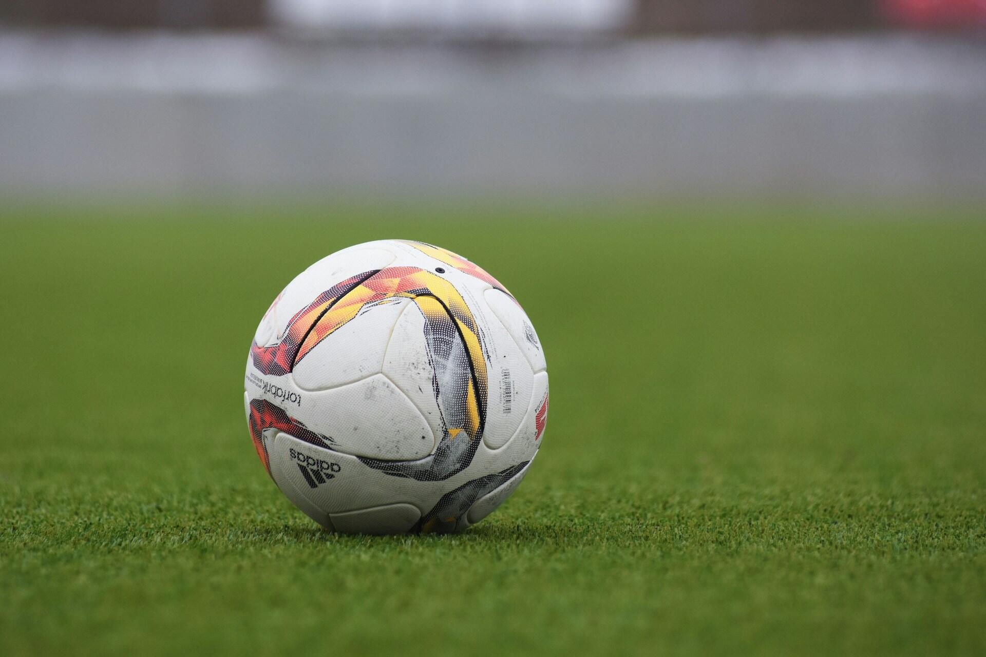 Football resting on a grass pitch with a blurred stadium background