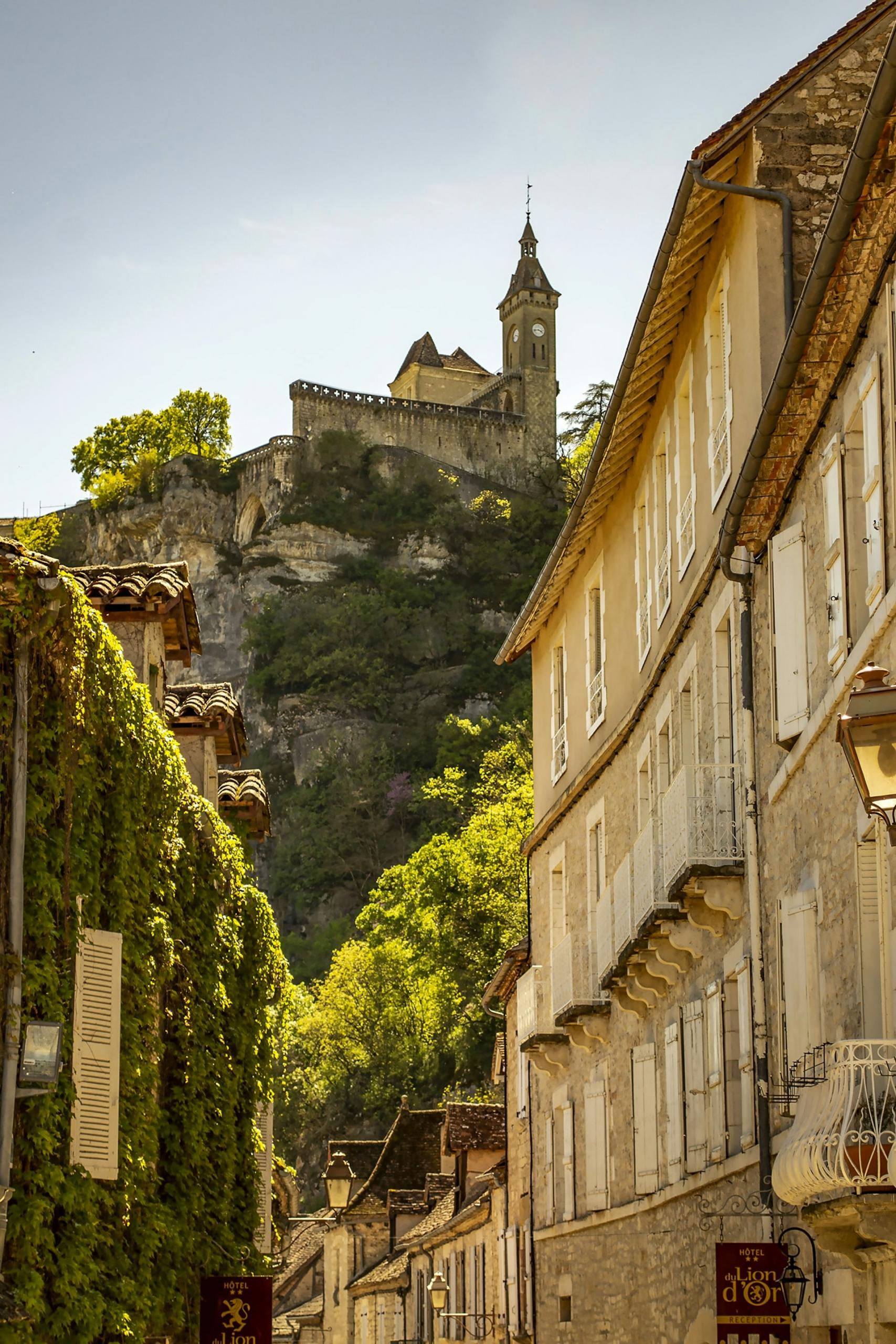 Stone buildings built into a hillside, which is topped with a spired building. 