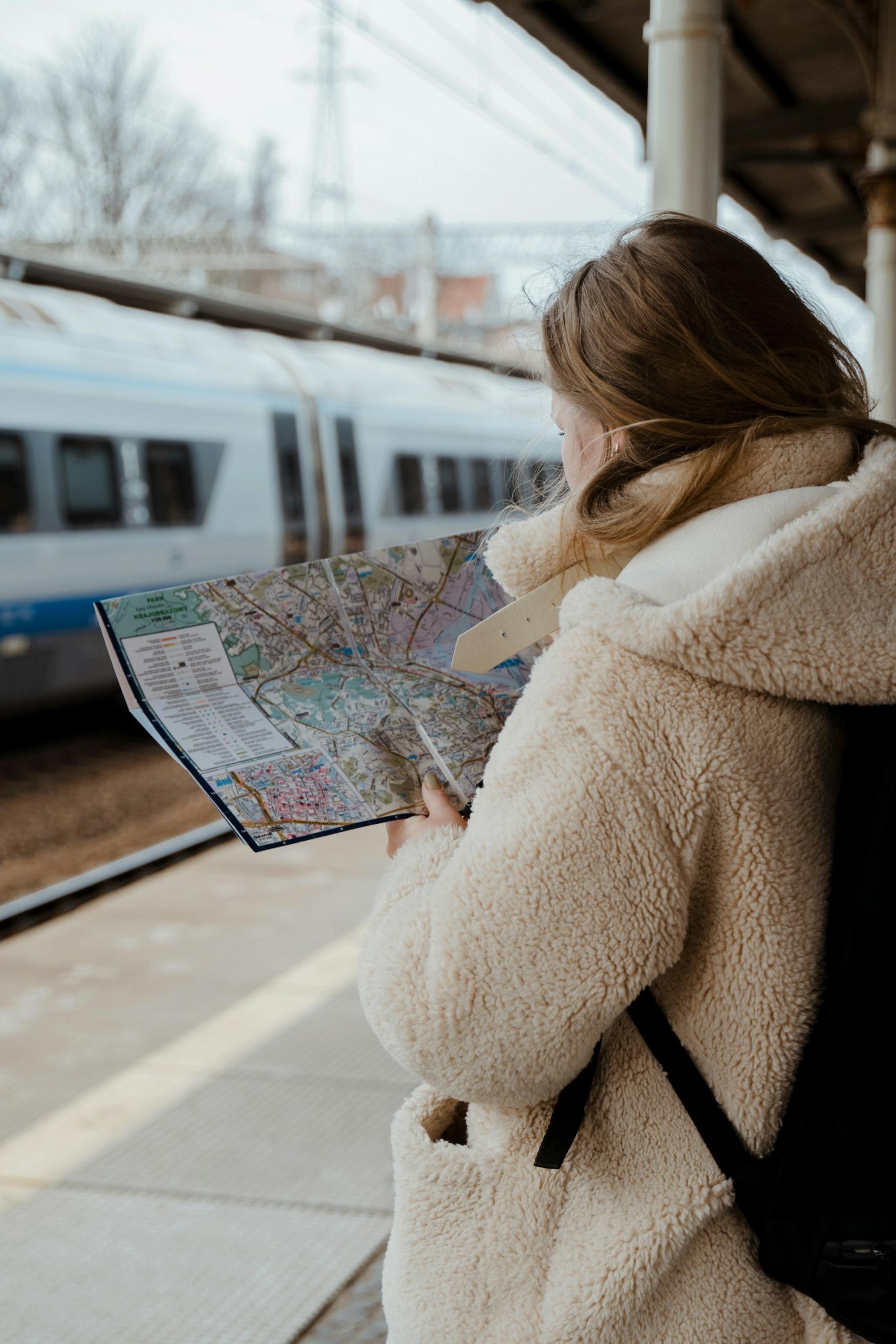 A person in a white fluffy coat holds a map on a train platform.