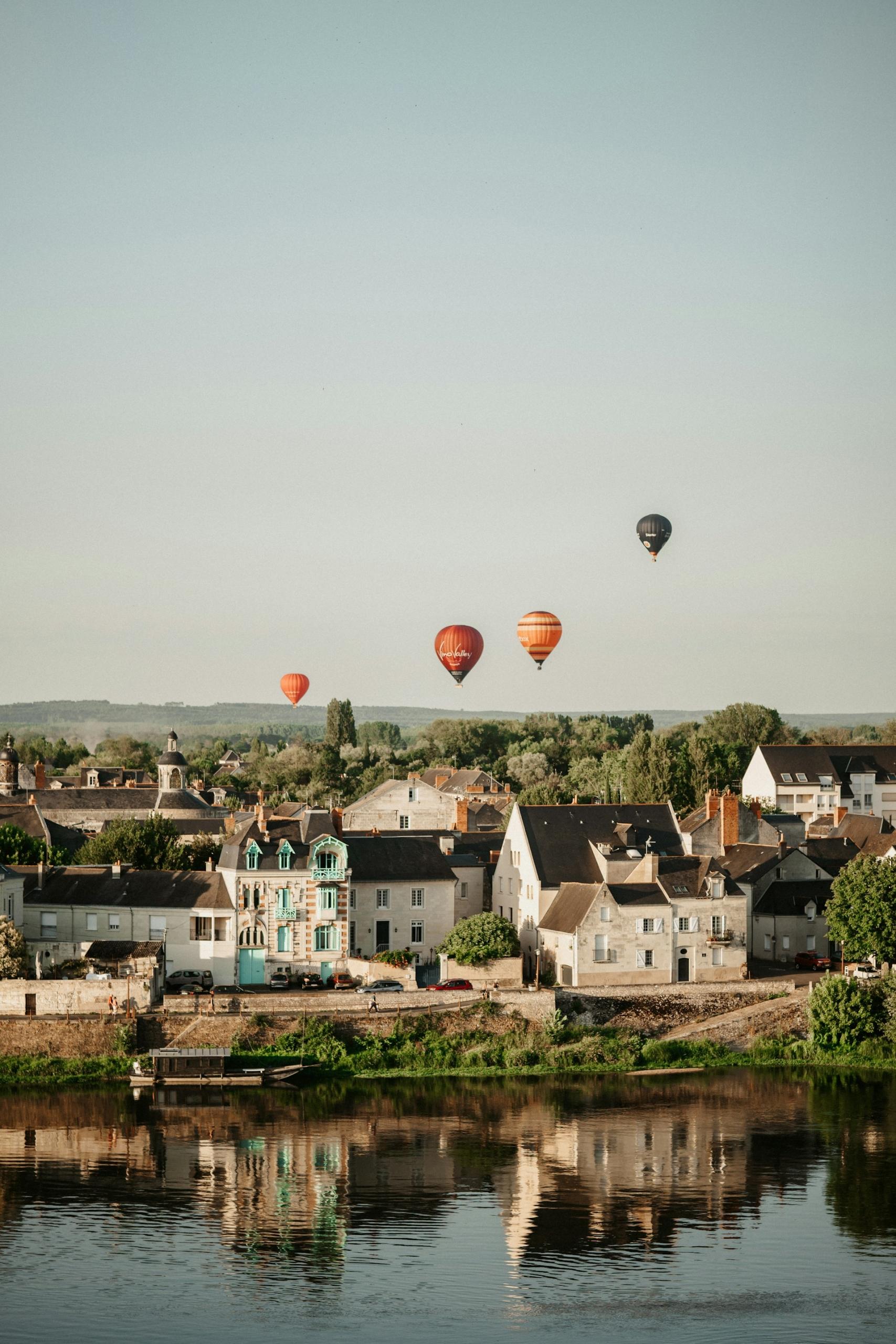 Hot air balloons drift over a town on a clear day. 