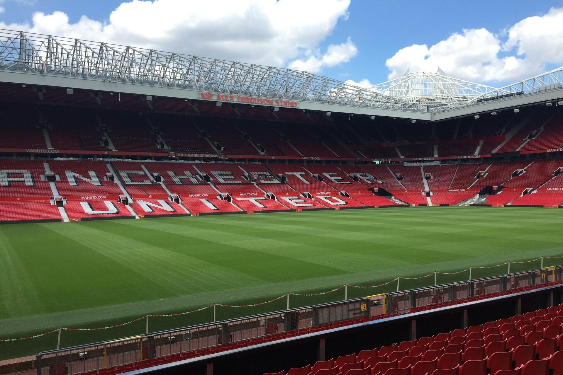 Wide view inside Old Trafford showing the pitch and red seating with Manchester United spelled across the stand