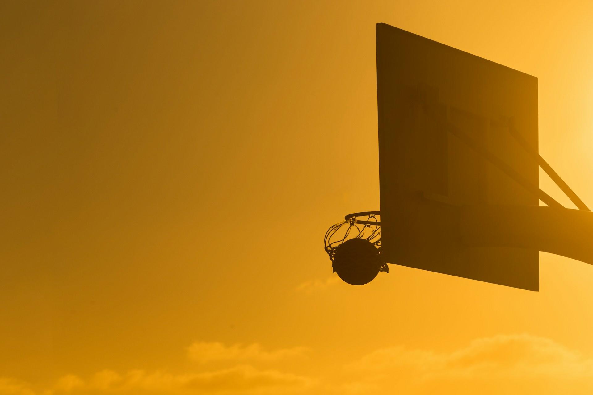 Basketball going through the net at sunset.