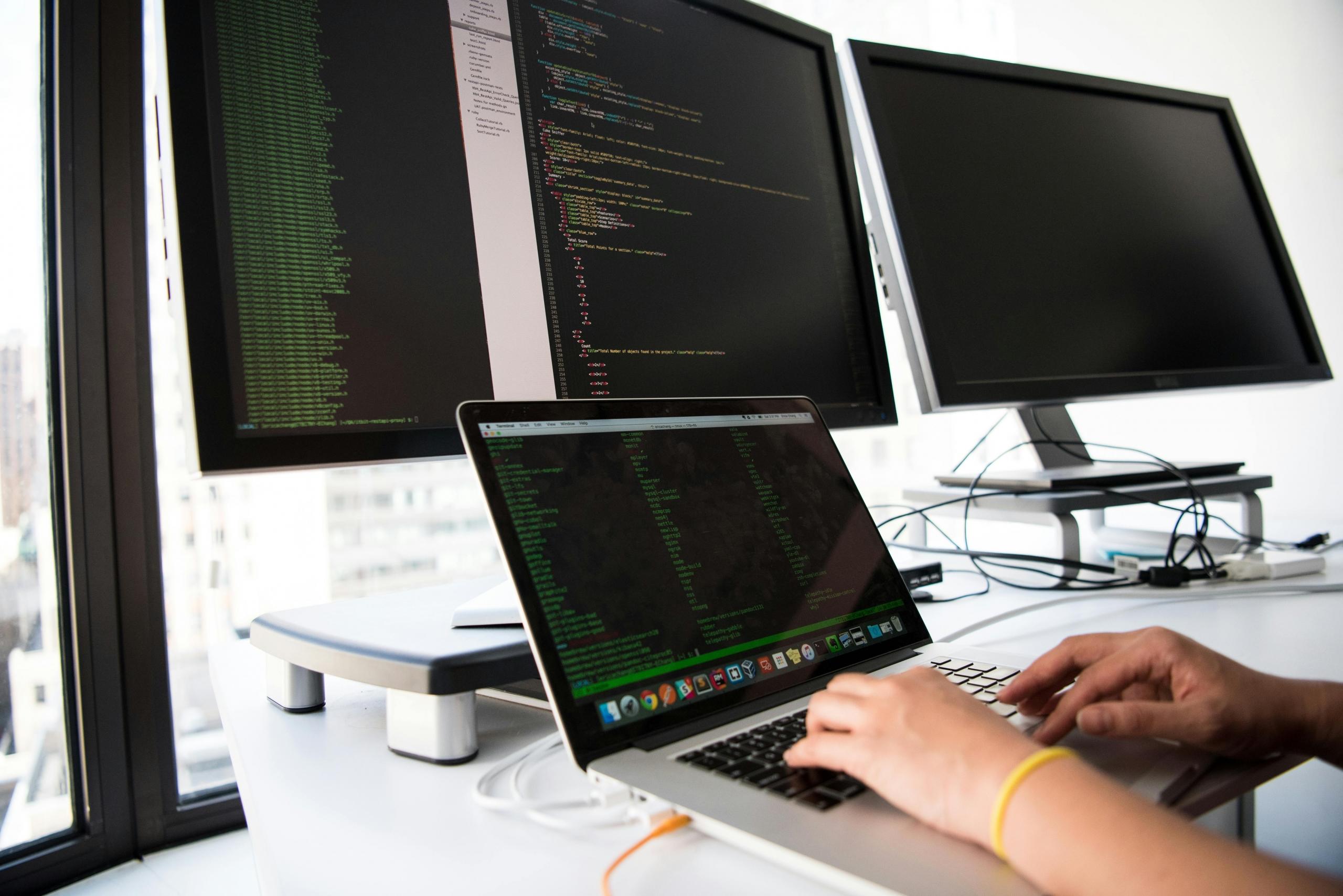 Three computer screens and one laptop coding
