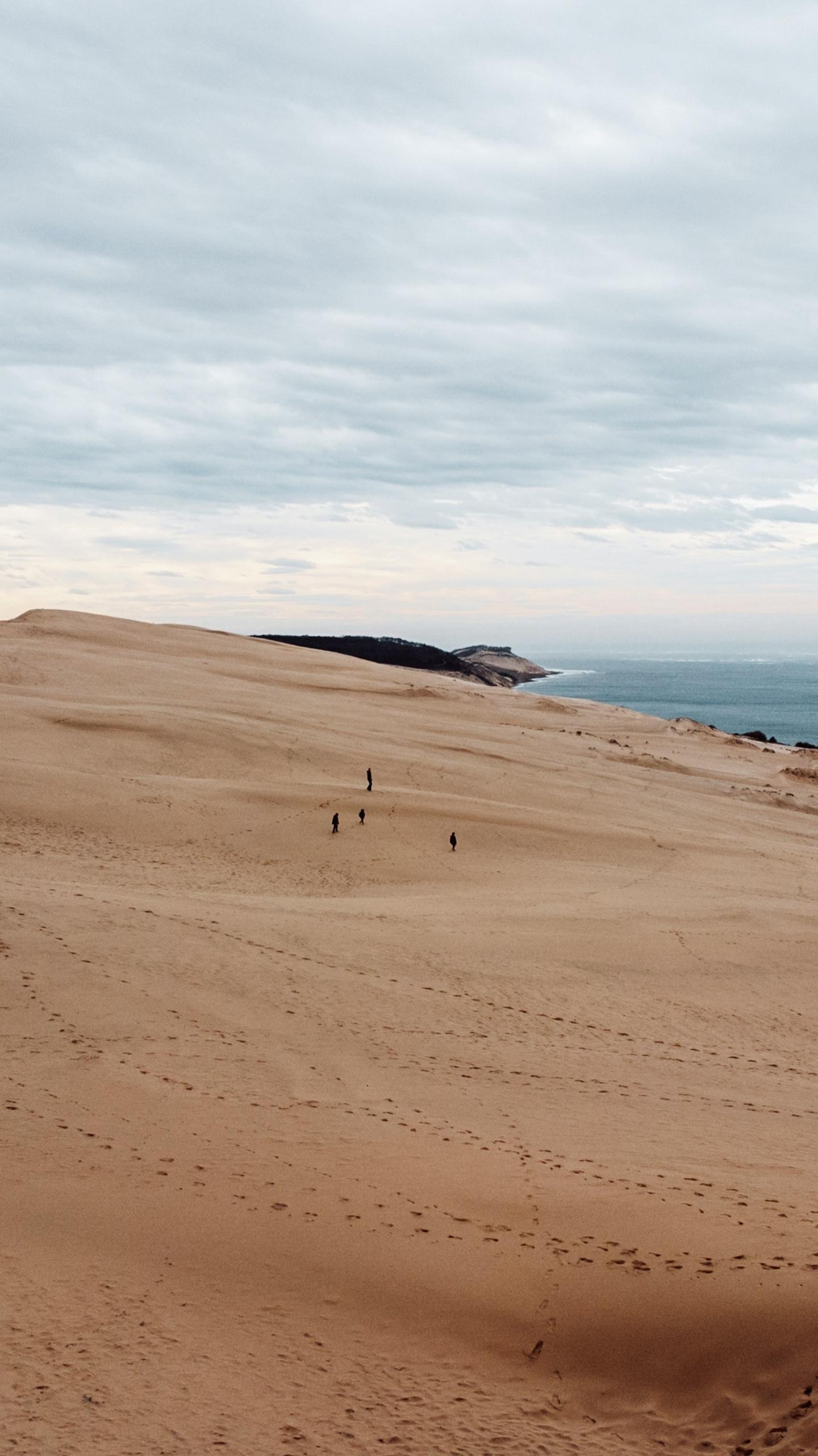 People walk along a large sand dune in daylight. 