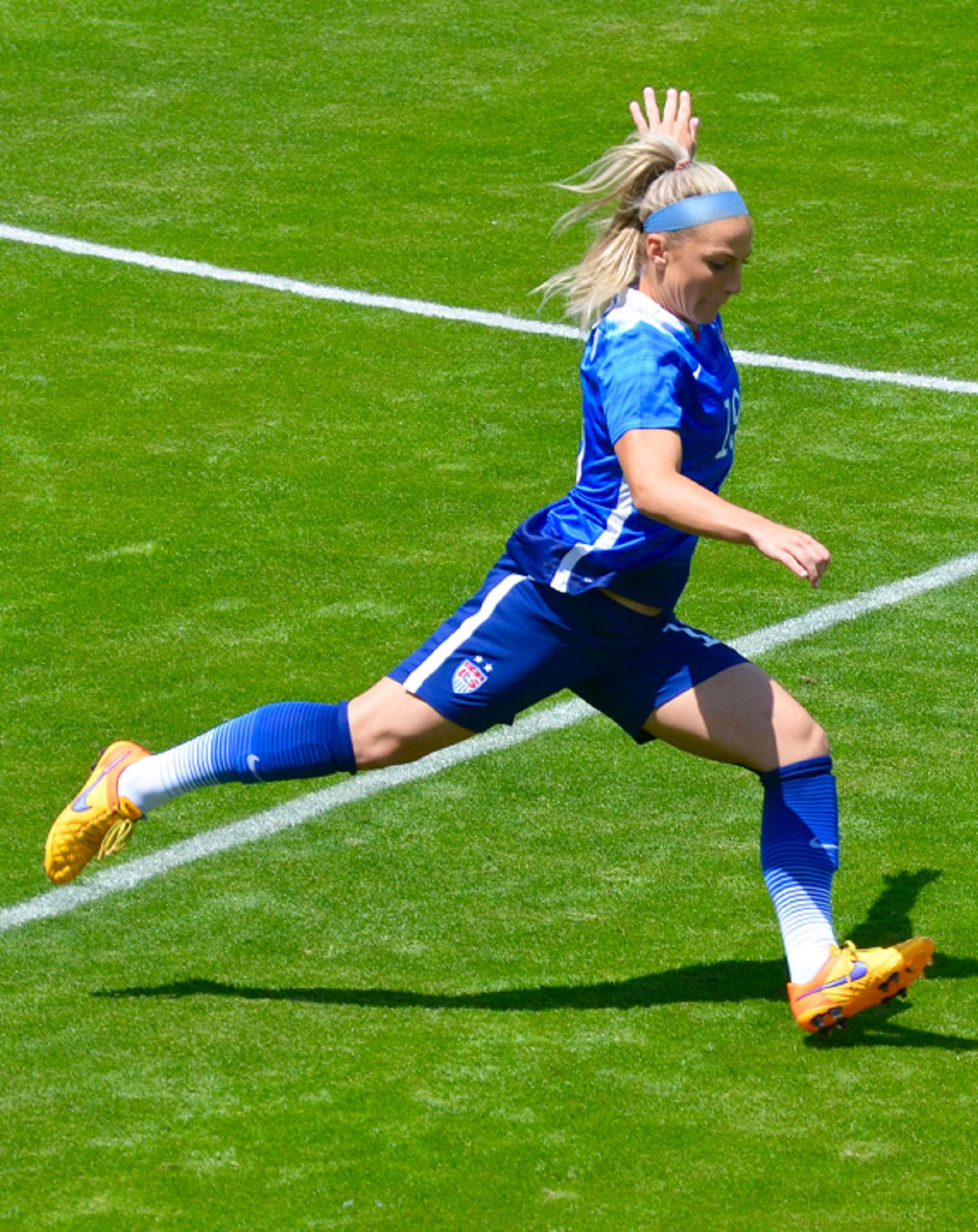 A woman in a blue soccer uniform prepares to kick the ball while running.