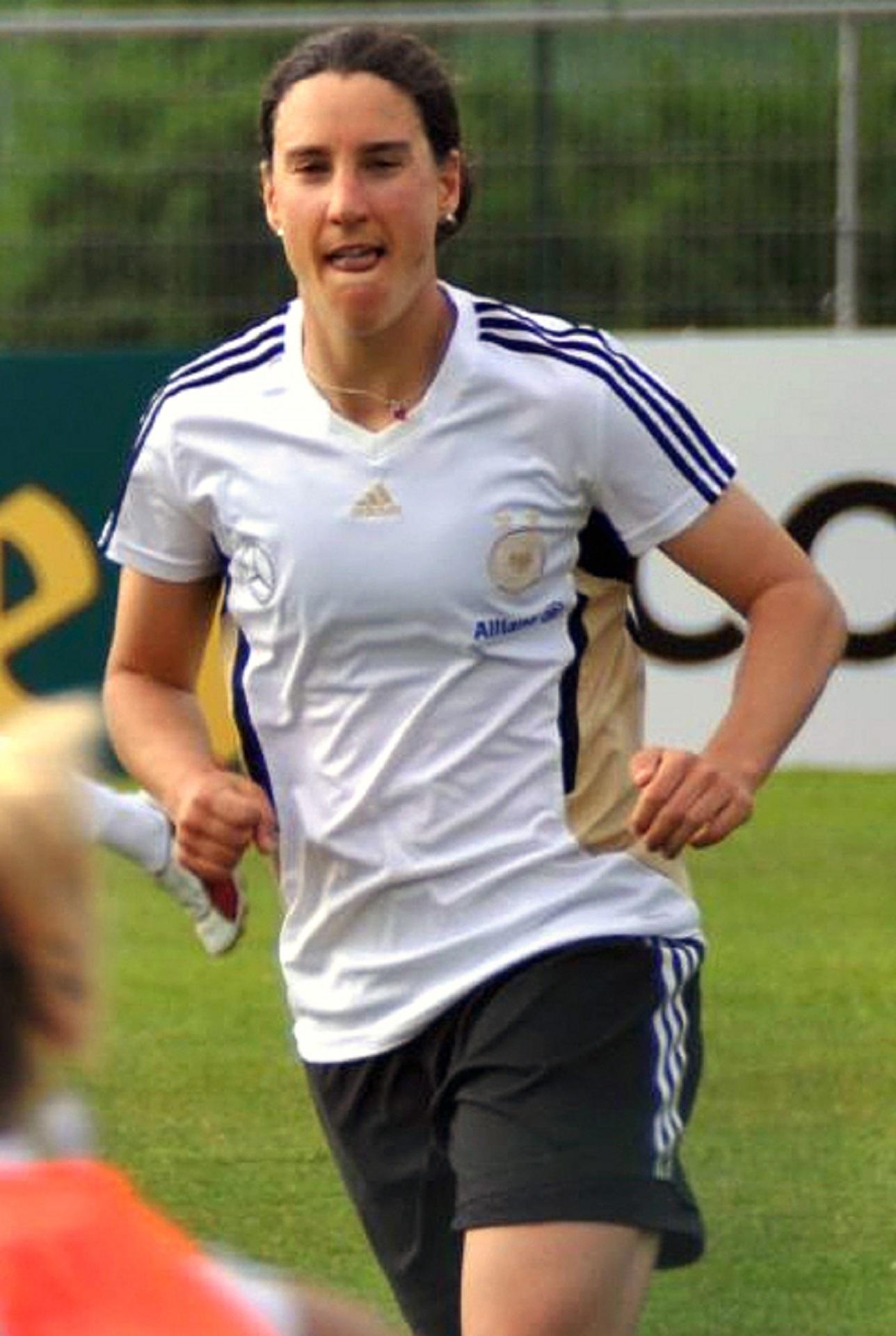 A person in a white top and dark shorts runs on a soccer pitch.
