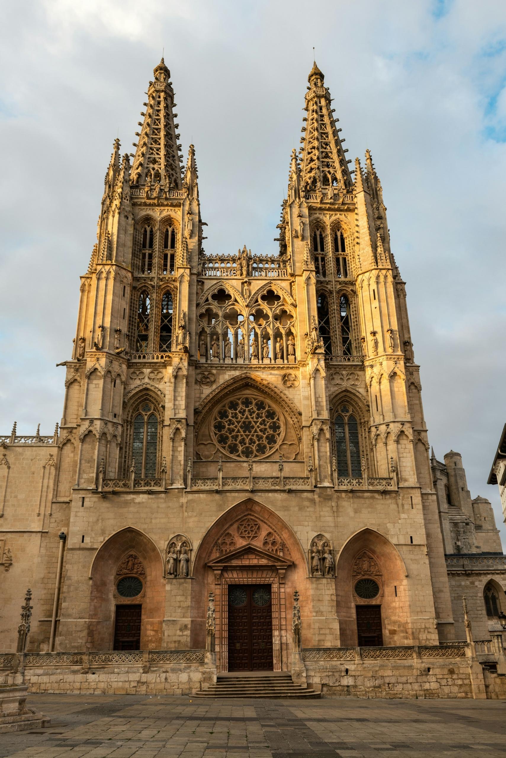 A tall stone building with two spires against a lightly cloudy sky.