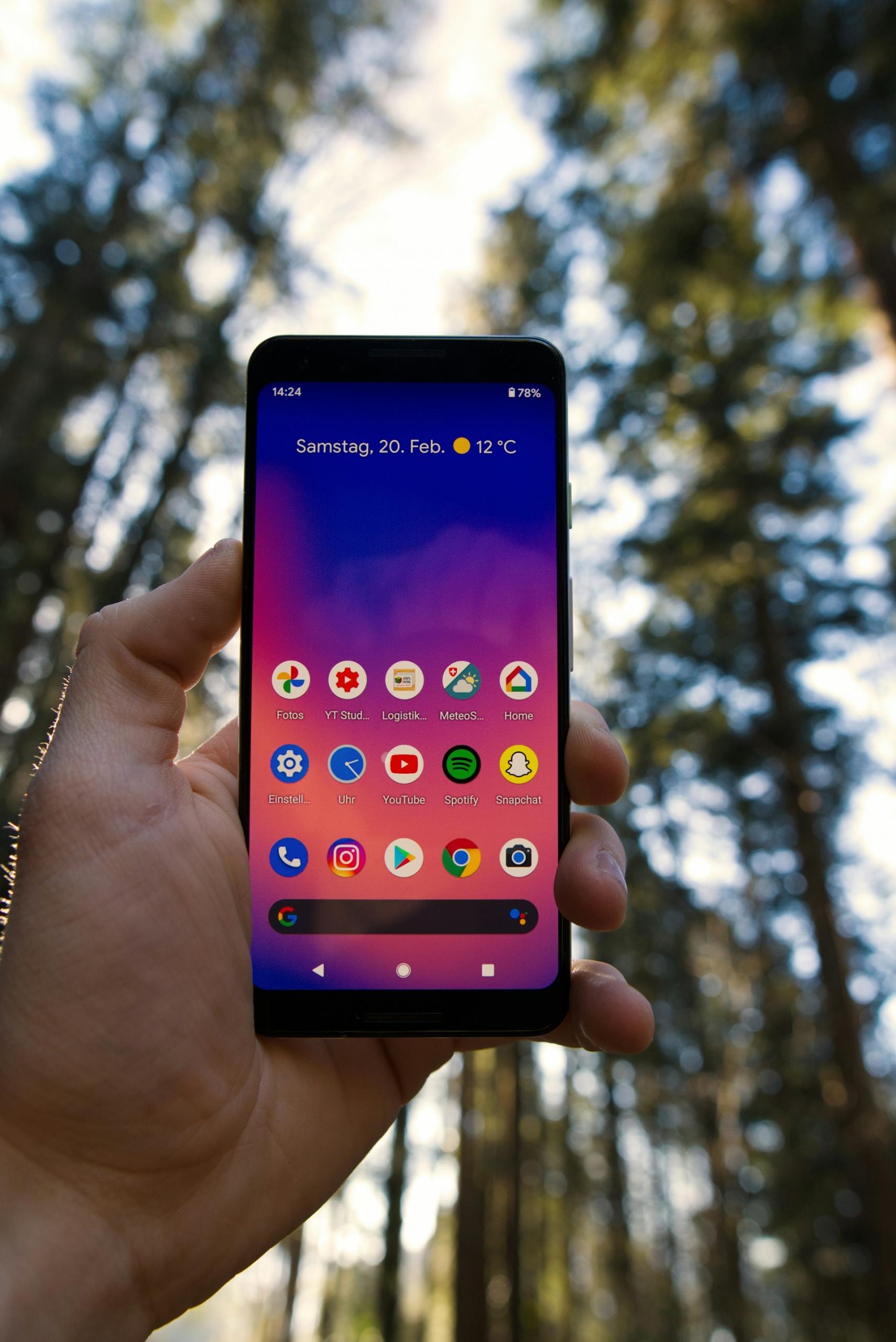 A person hold up their smartphone in a wooded area. 