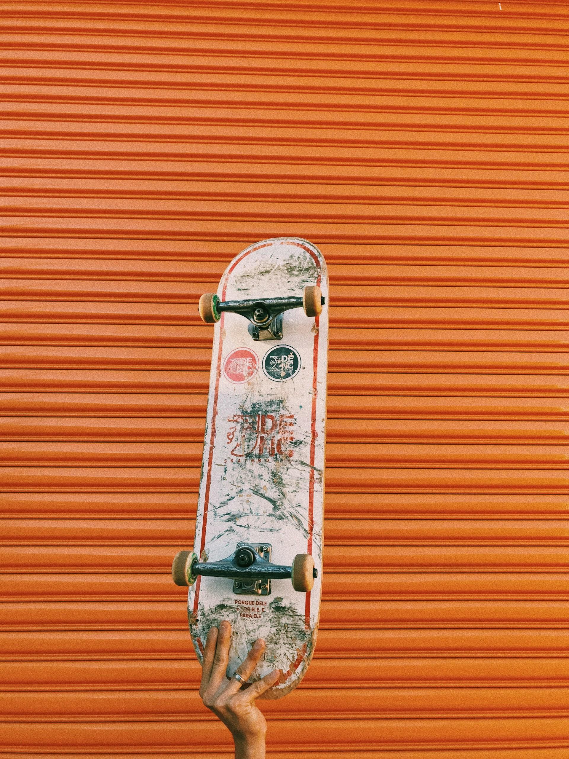A person holding up a skateboard by the tail, showing the art on the underside of the deck