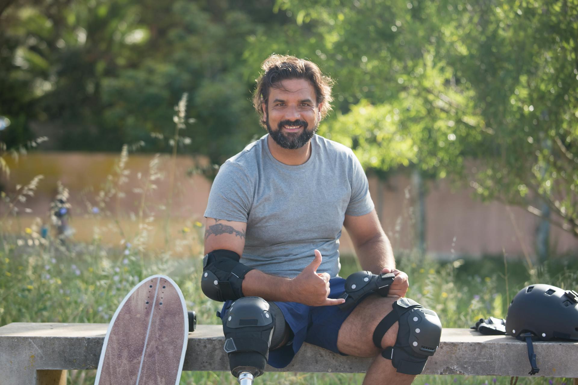 A man wearing skateboard safety gear, smiling, and giving a "shaka" or "hang loose" hand sign.
