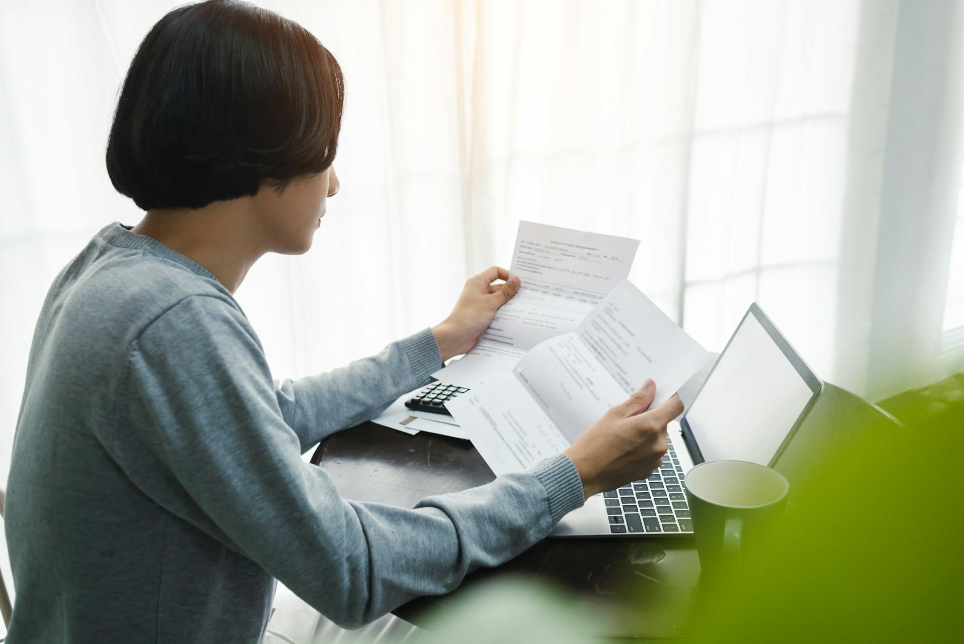 A person in a grey jumper looks at the papers they're holding.