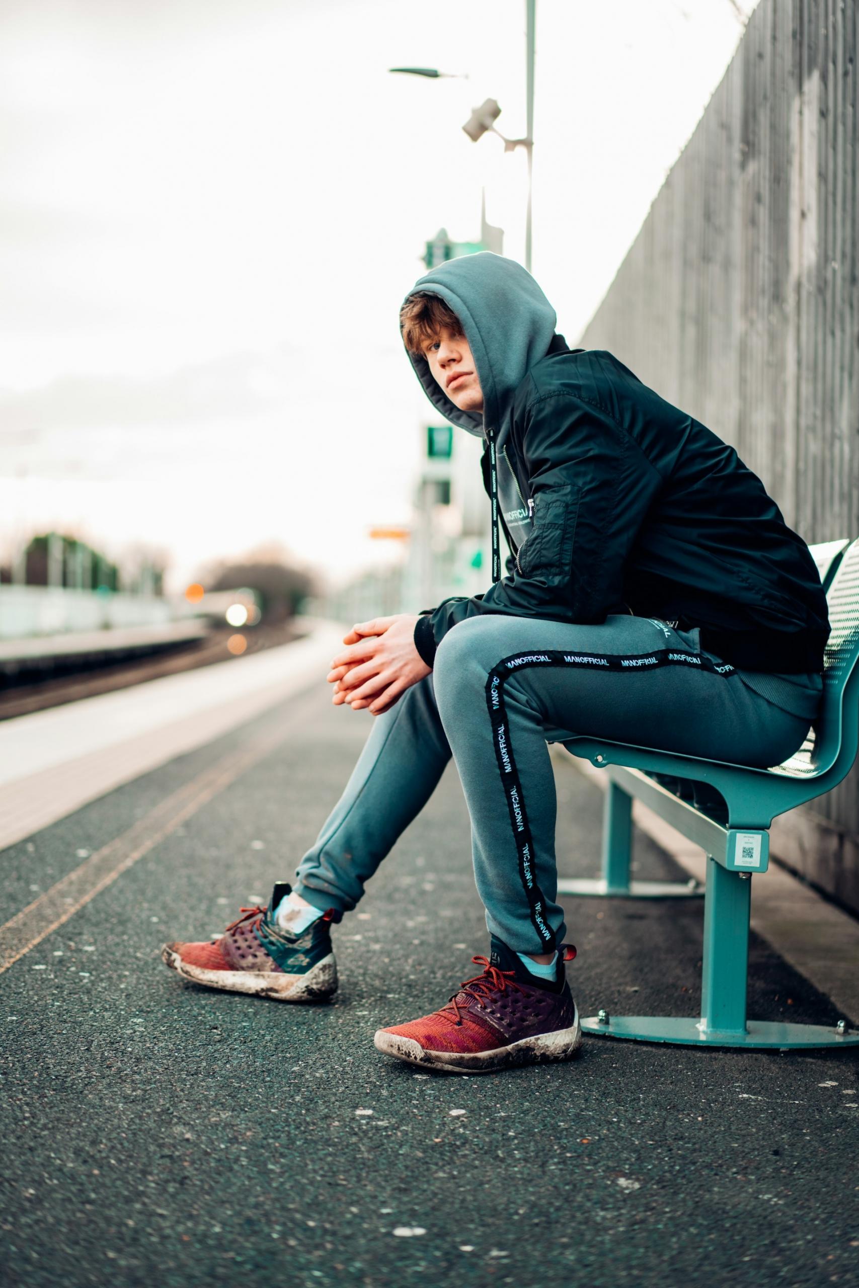 A person wearing a grey hoodie sits on a bend during daylight. 