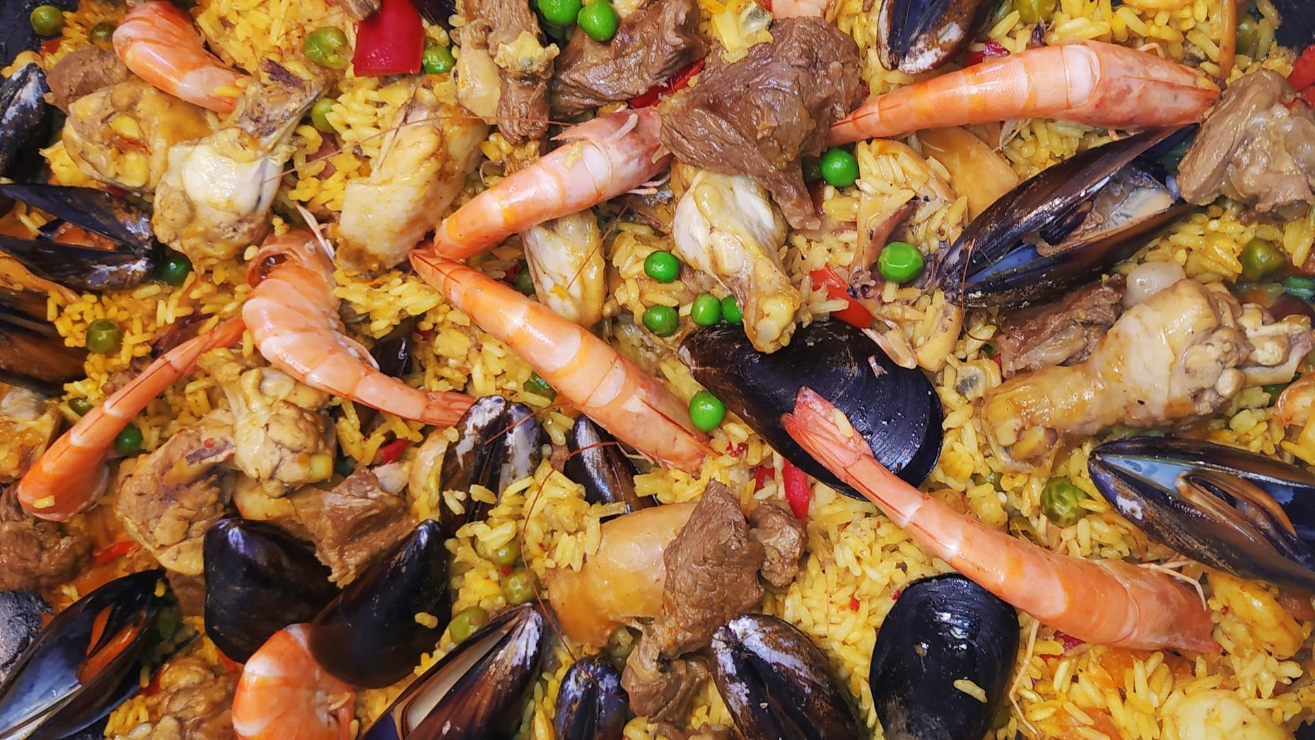 A plate of typical Spanish food such as shrimp, mussels, rice and peas. 