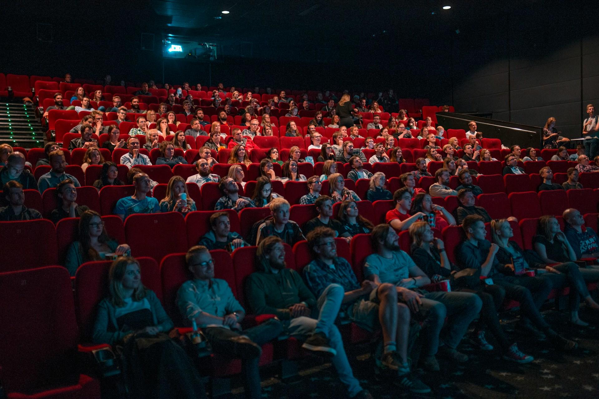 People sit in a cinema with red chairs, watching a film.