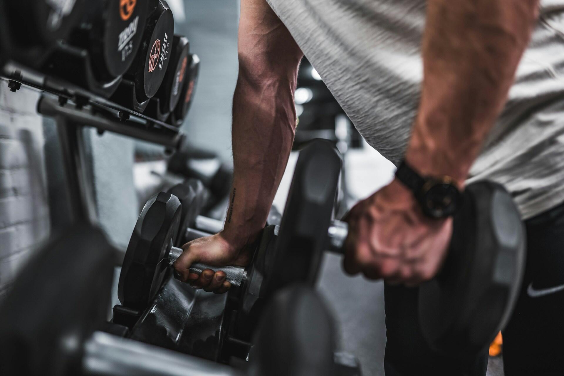 Person lifting two dumbbells from a rack in a gym