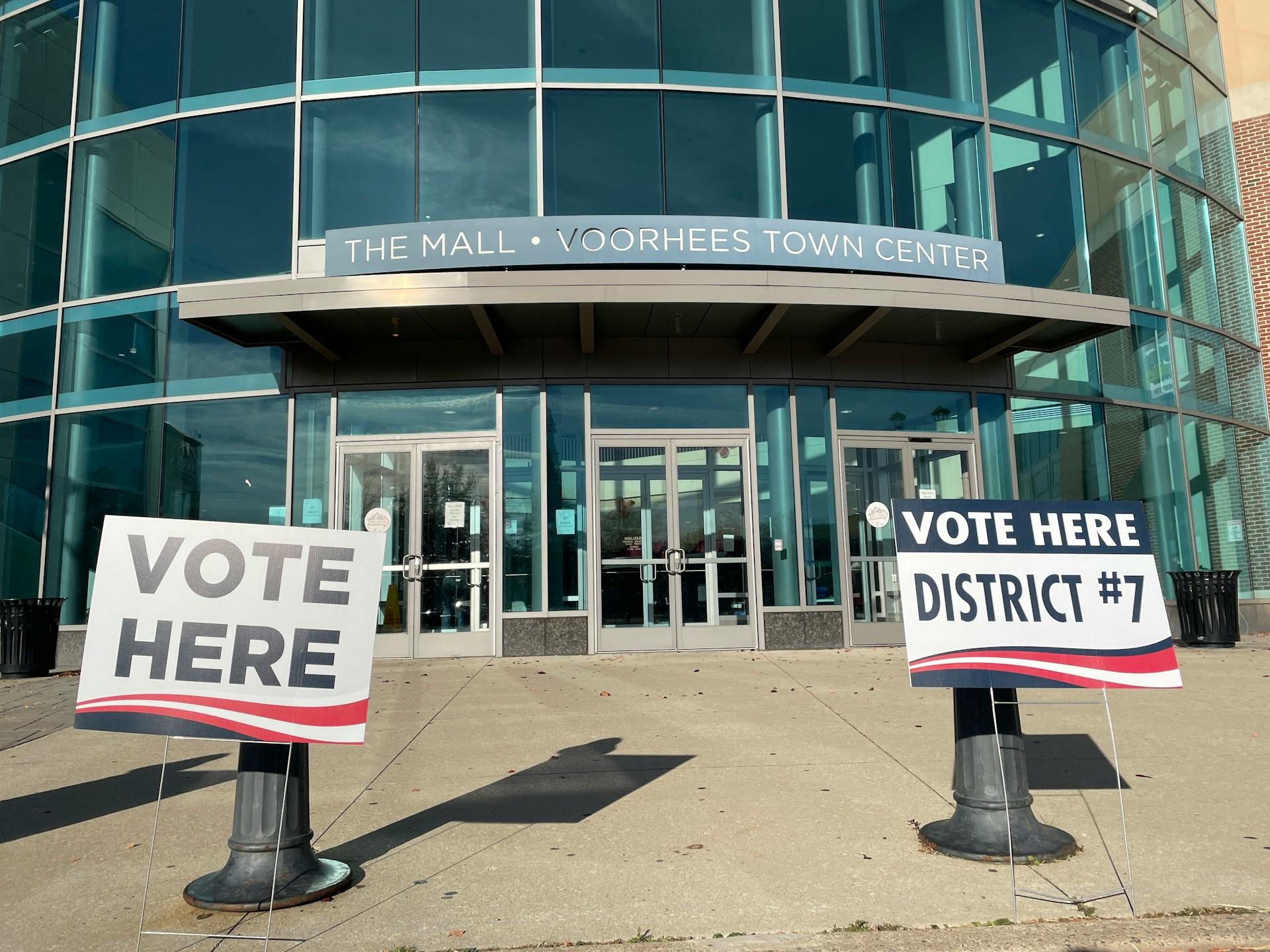 Voting signs outside a glass facade building on a sunny day.