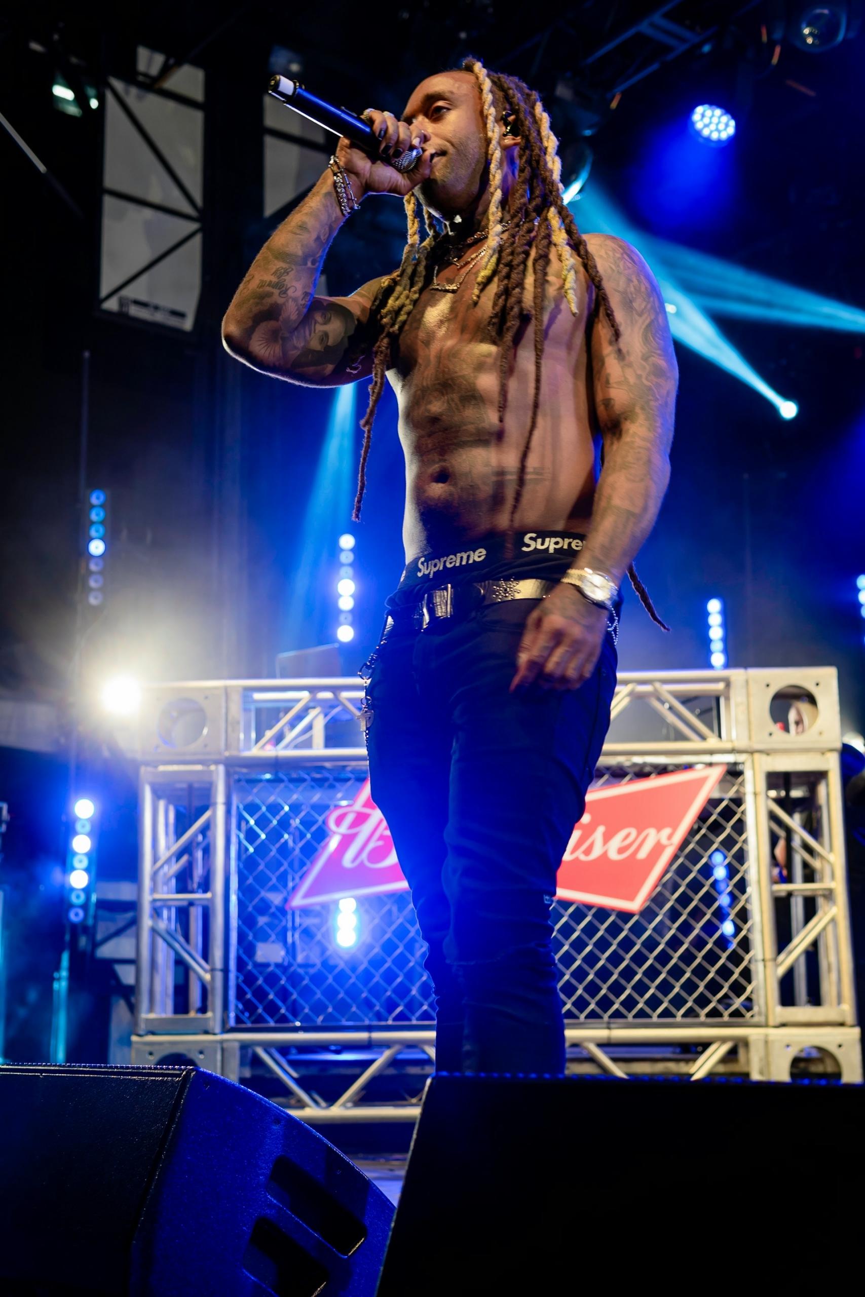 A shirtless man with dreadlocks on stage. 