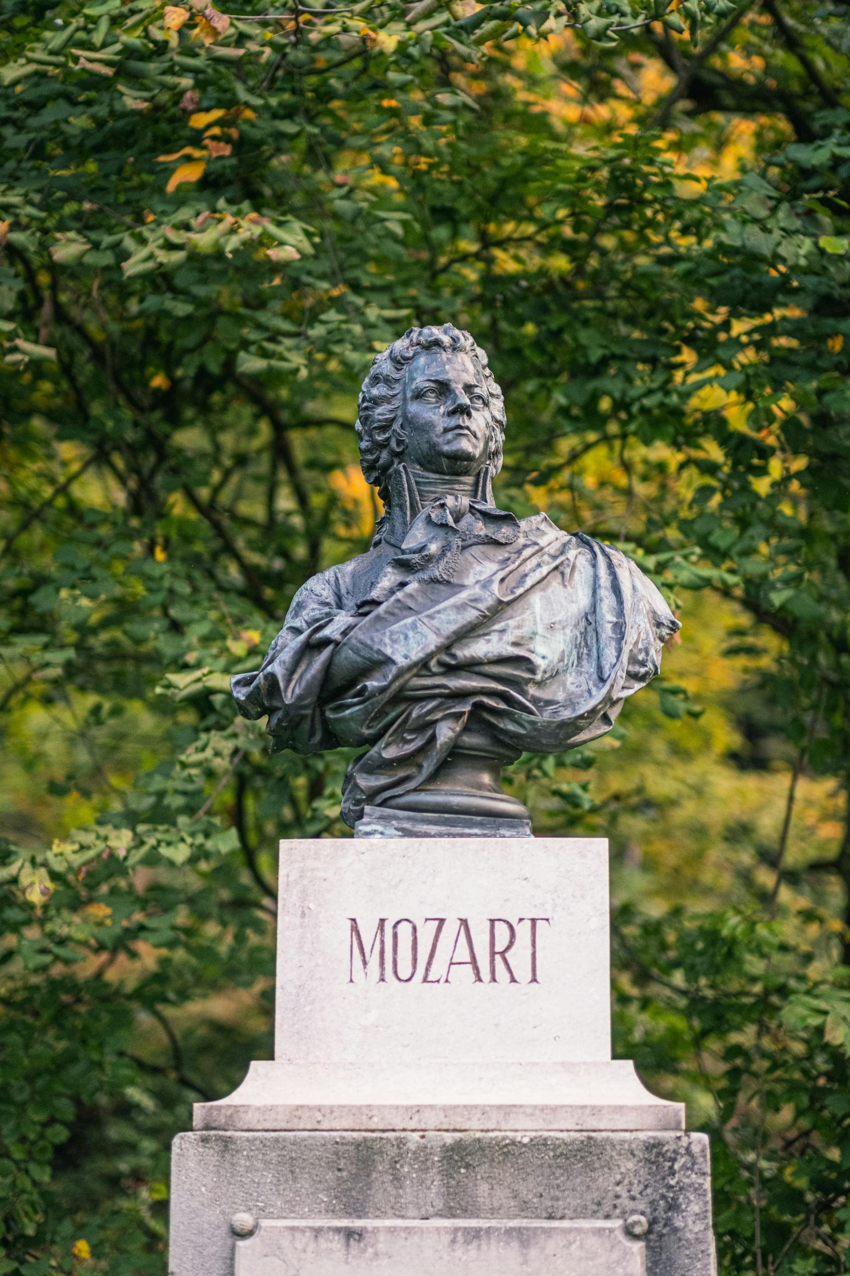 A bust of Mozart on a plinth in a park. 