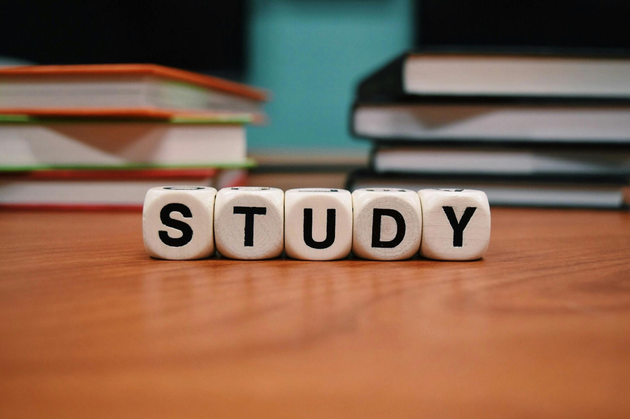 dice spelling 'STUDY' on a desk in front of a pile of books