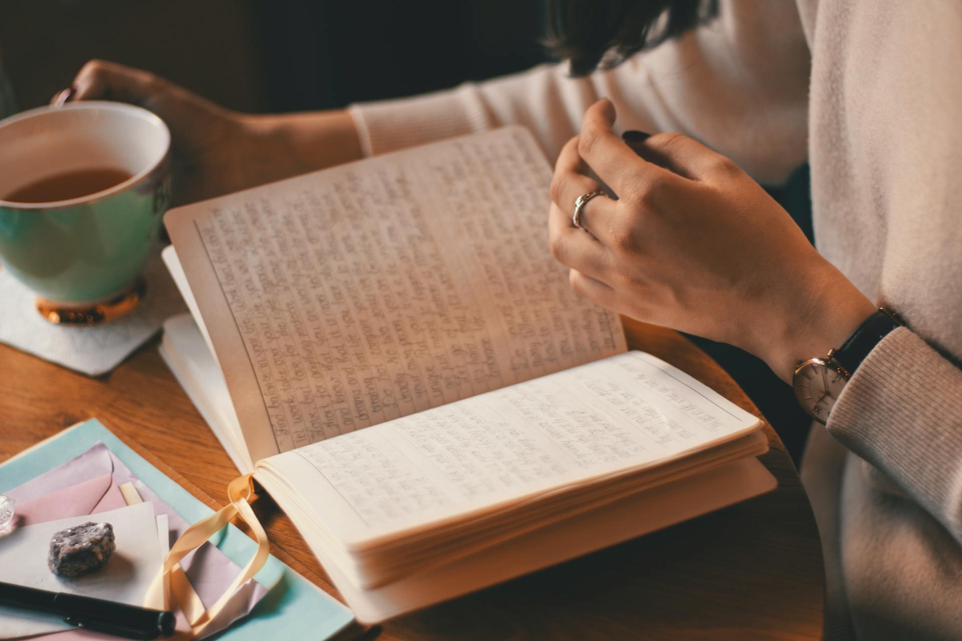 Photograph of someone reading a notebook and drinking a cup of coffee.