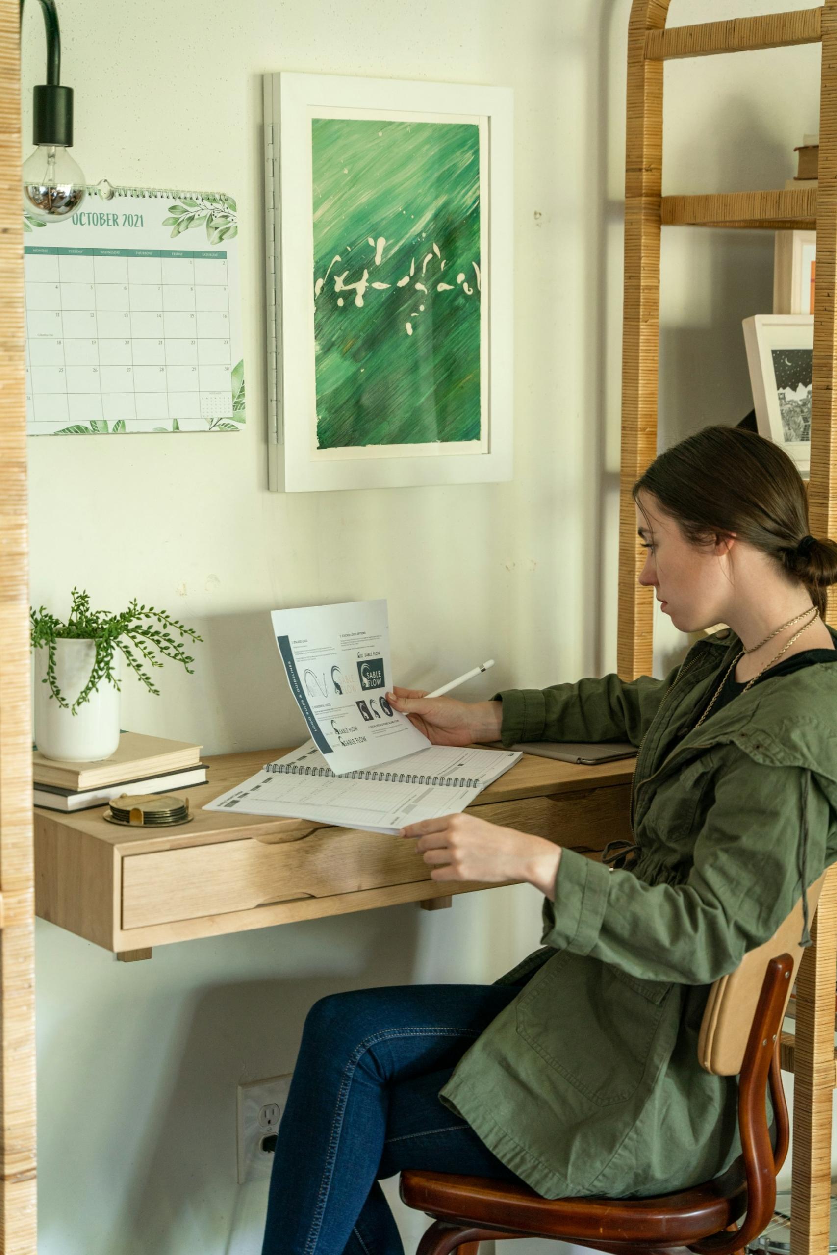 A person wearing green sits at a desk in a brightly-lit room. 