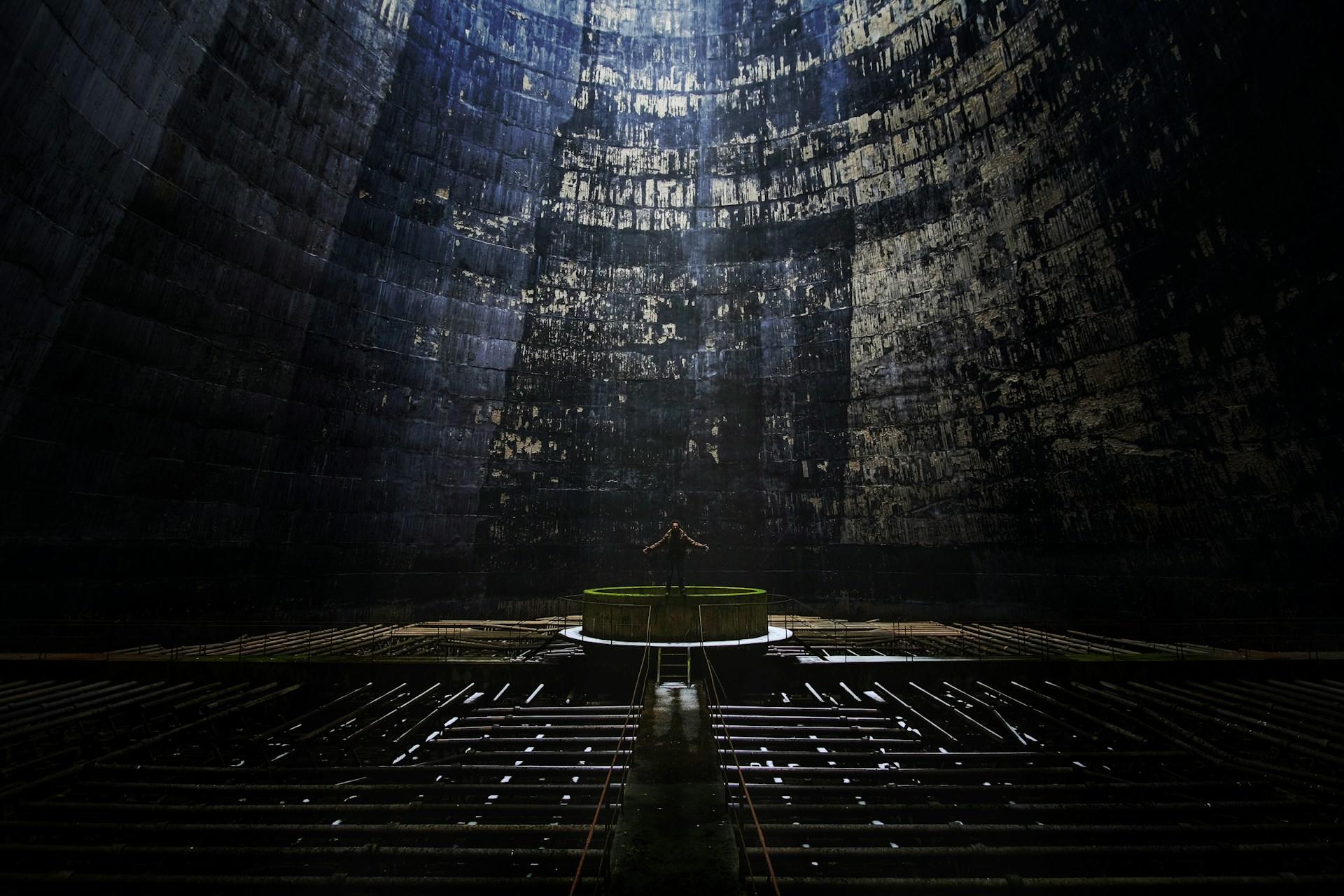 A person stands on a platform with their arms spread in a large, gloomy setting.