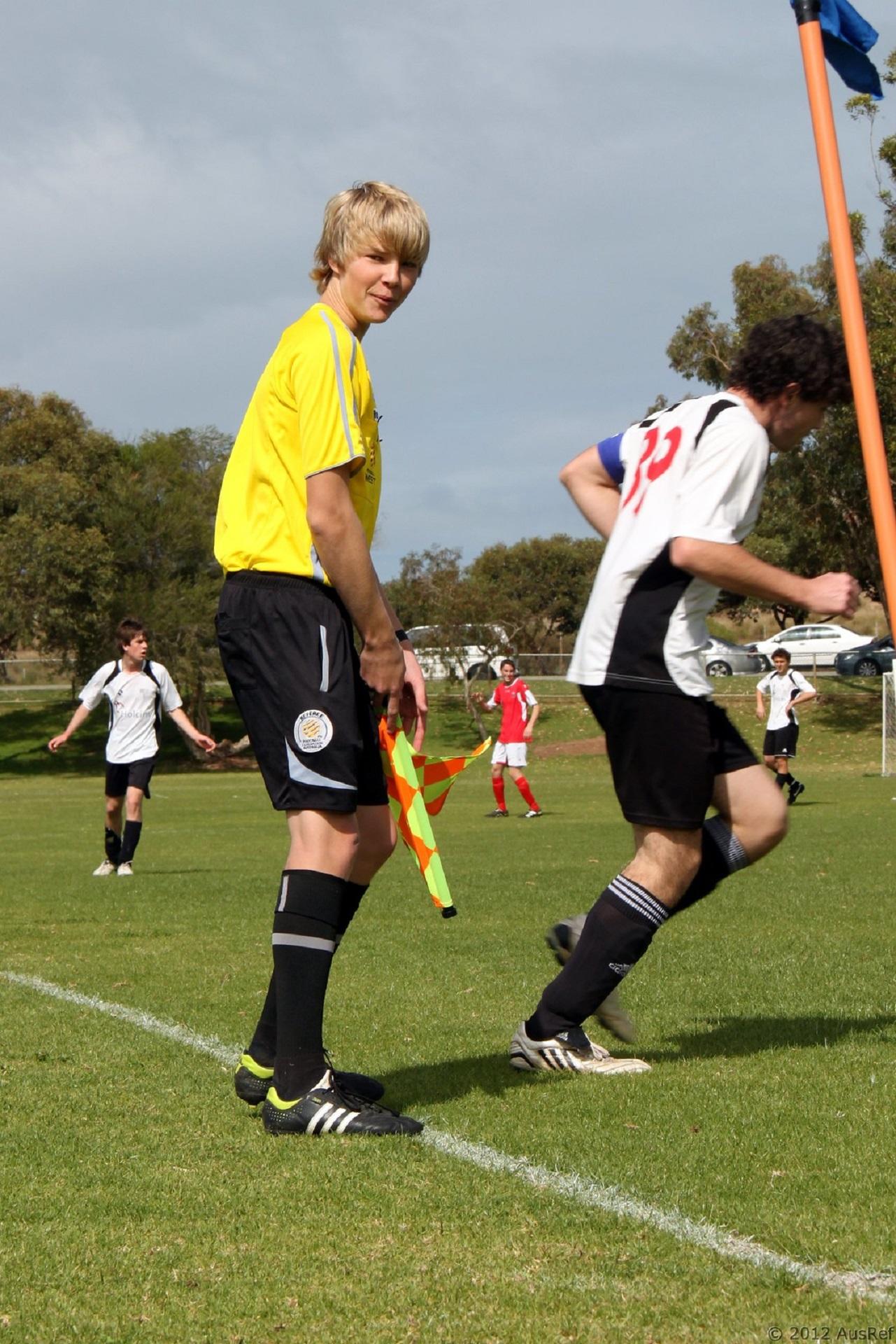 A person in a yellow sports jersey stands next to a soccer pitch on a sunny day.