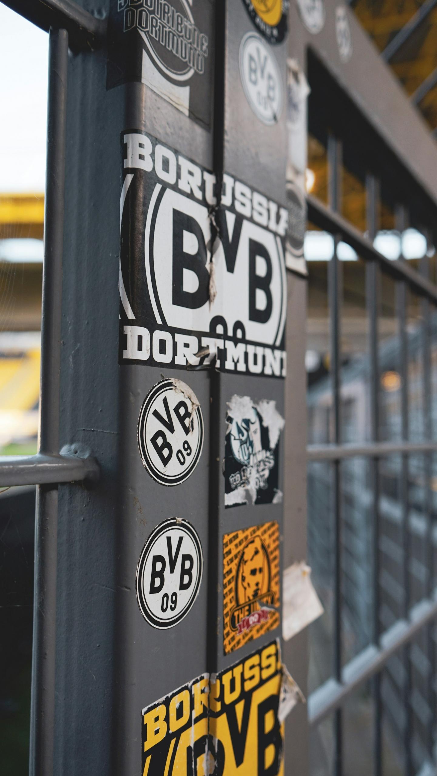 Bundesliga club stickers adorn a metal post near a football pitch. 